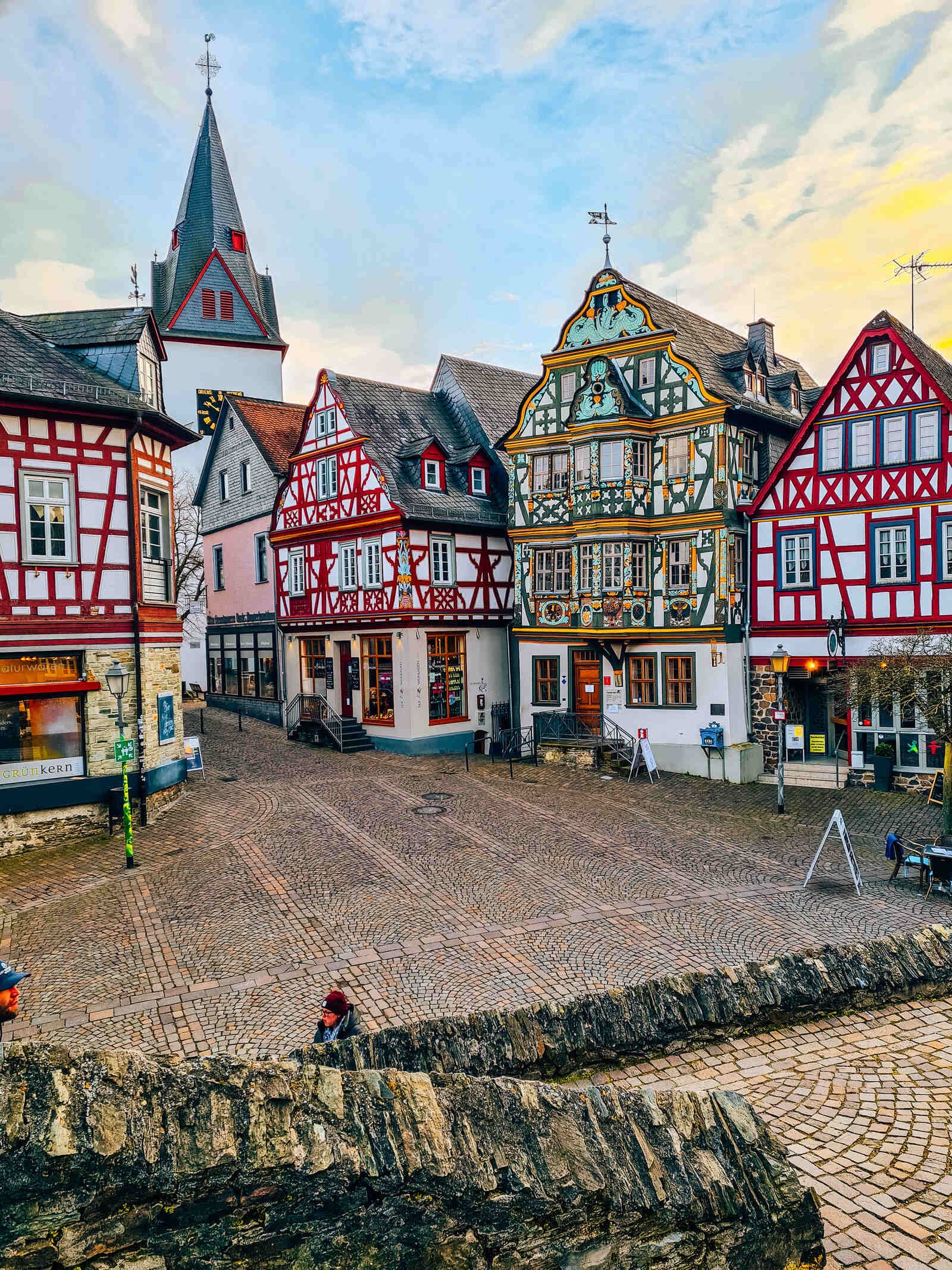  An open town square with many colourful ornate traditional German buildings and the top of a church in the distance 