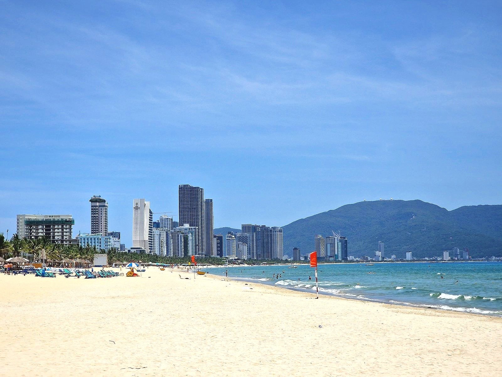 a white sandy beach and blue sea with the city skyline of Da Nang in the distance