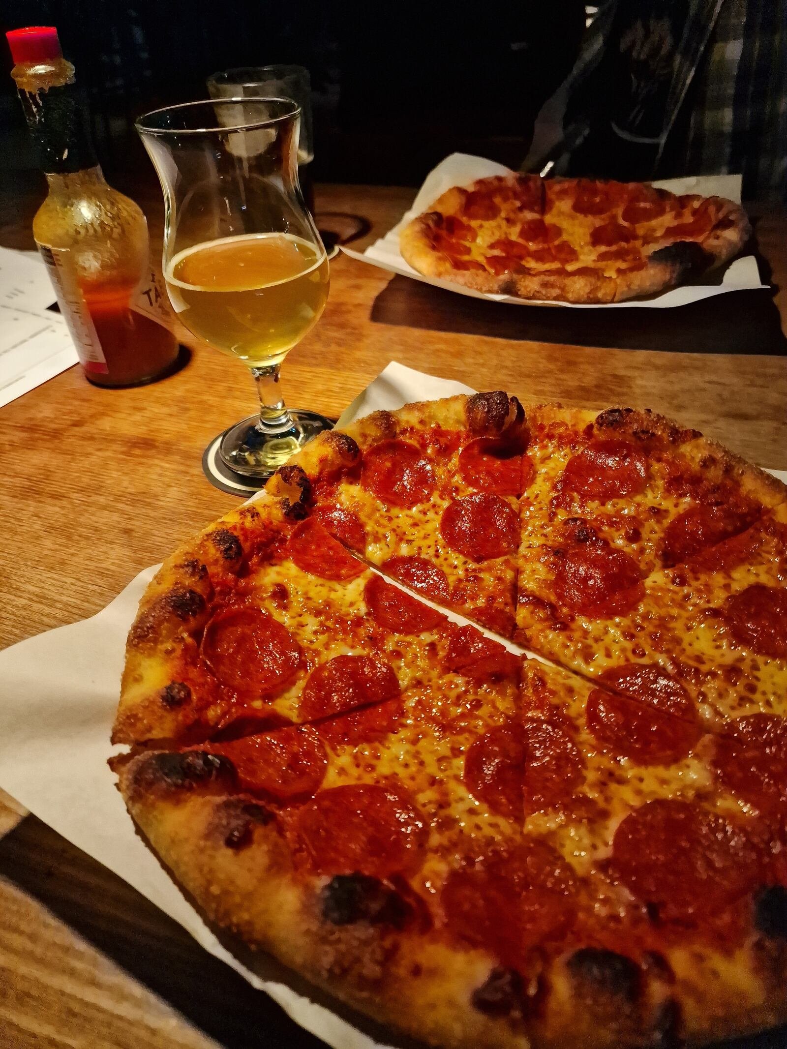 Two large pepperoni pizzas next to a glass of beer