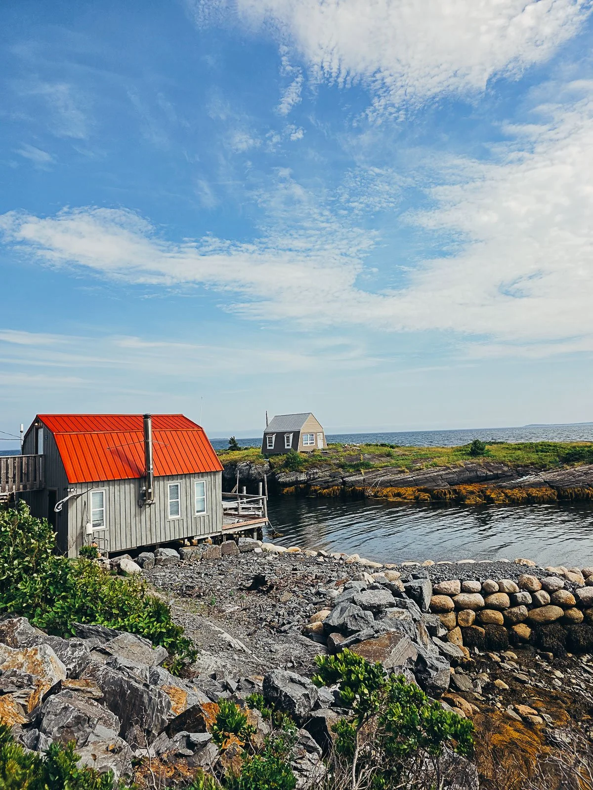 a small inlet with a house on the nearside and the far side. Both are saltbox style with the closest one having a red roof.