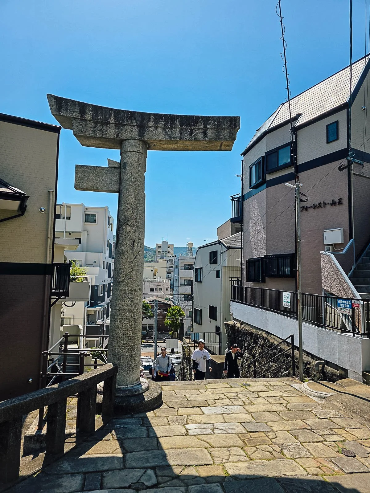 The remains of a torii gate in Nagasaki with only half still standing at the top of a stairway surrounded by residential buildings