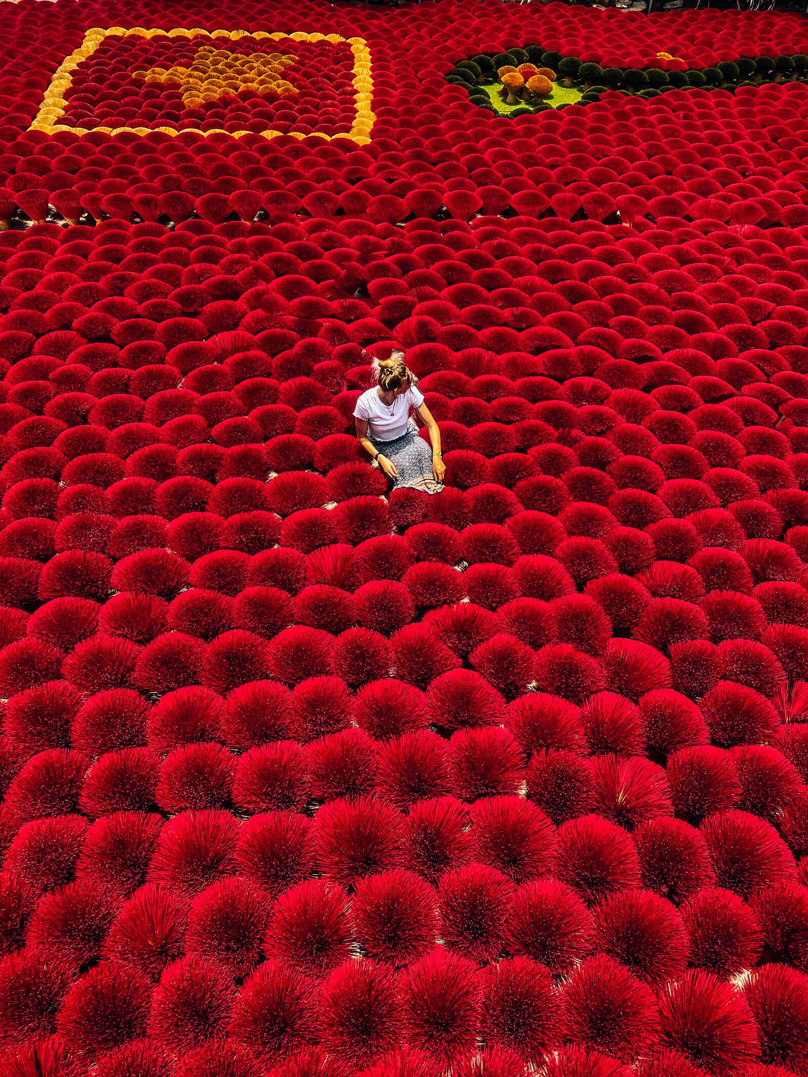 Helena in a cone hat sitting in the middle of a sea of red bundles on incense