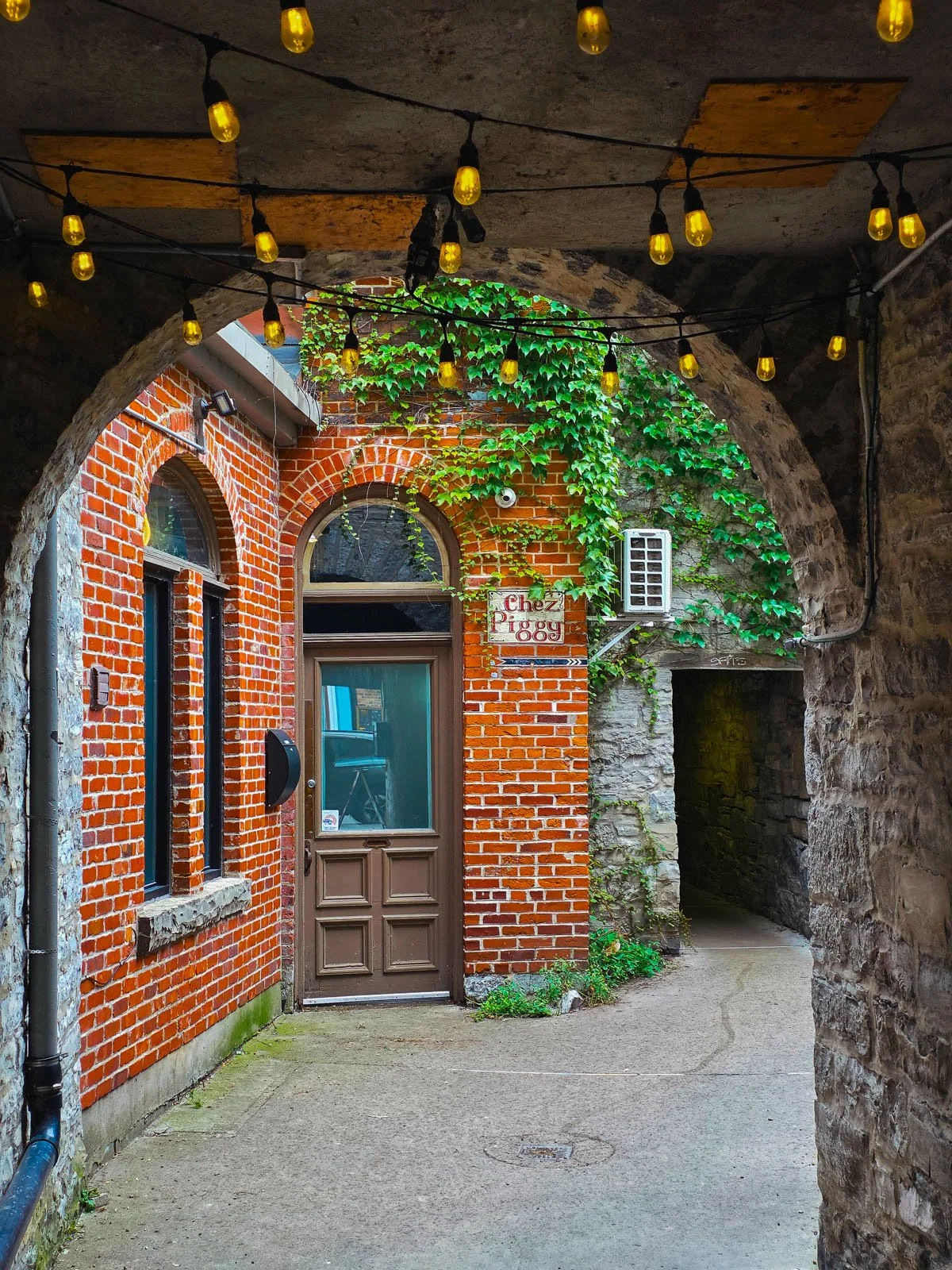 A red brick restaurant in a stone courtyard, down an alleyway strung with string lights