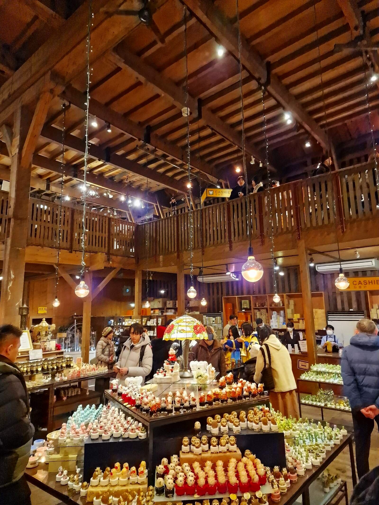 a large wooden room with vaulted ceiling and upper balcony. Large shop displays with people milling around the tables with small products on