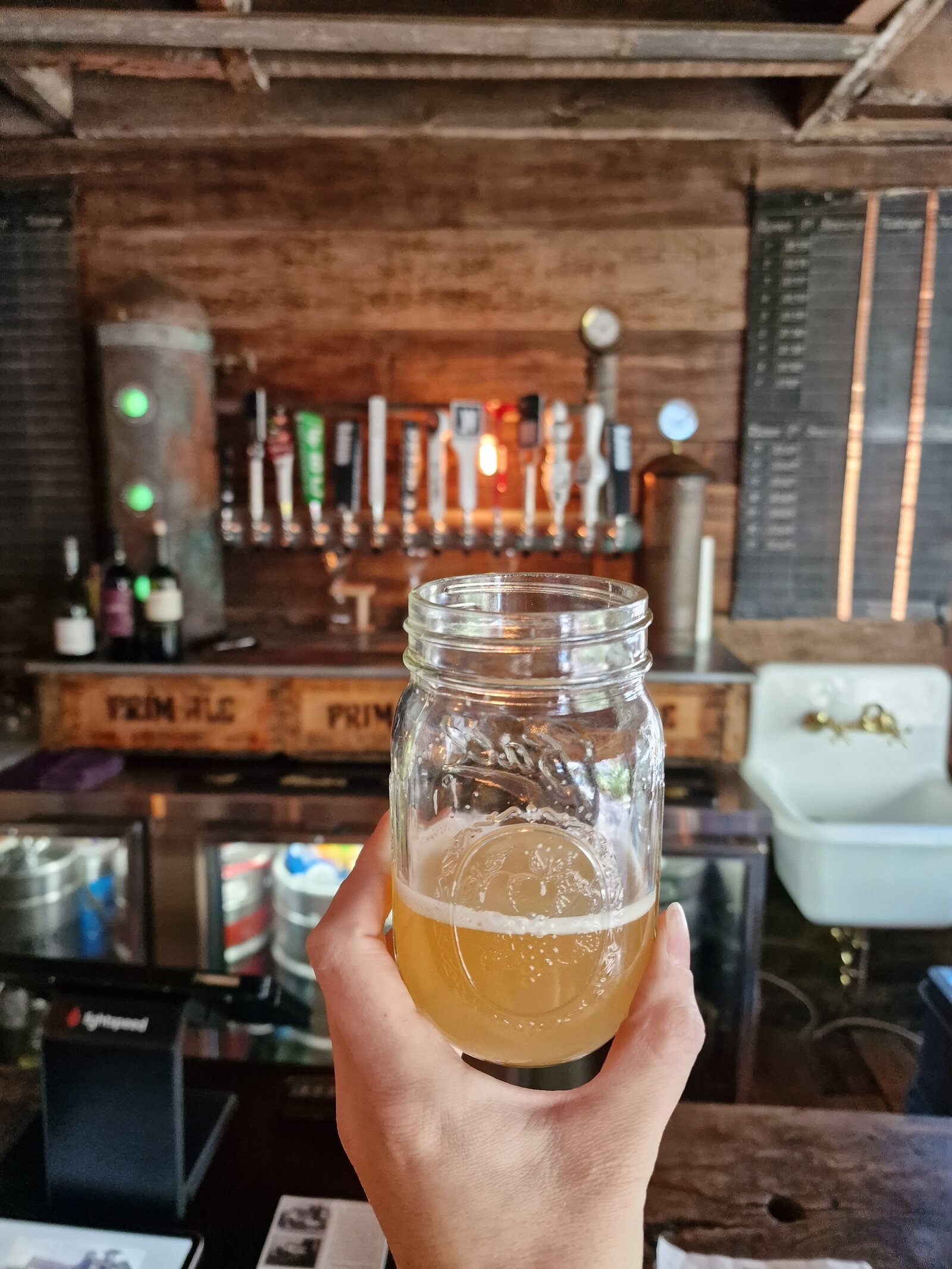 beer in a mason jar held in front of a rustic wooden wall with beer taps on