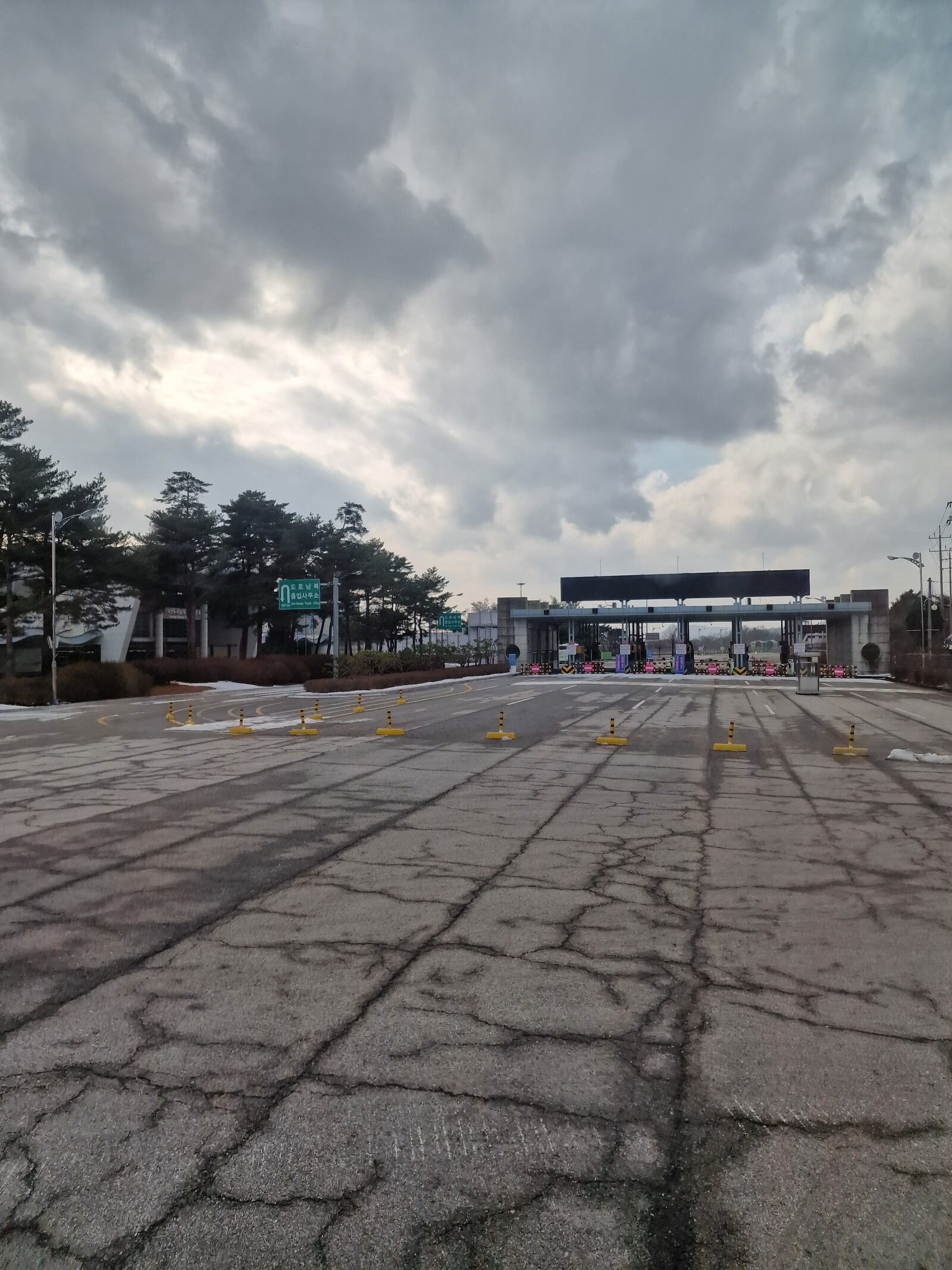 a large grey asphalt area leading to an empty border crossing gate