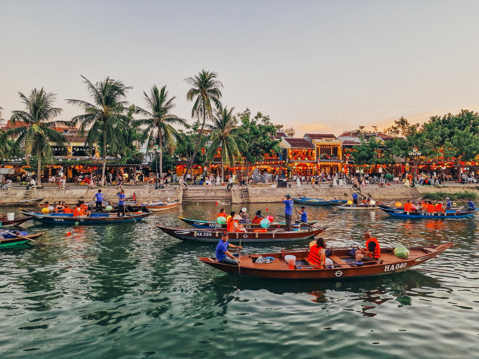 traditional wooden boats decorated with lanterns on the river at dusk in Hoi An, streets with lanterns in the backgroun