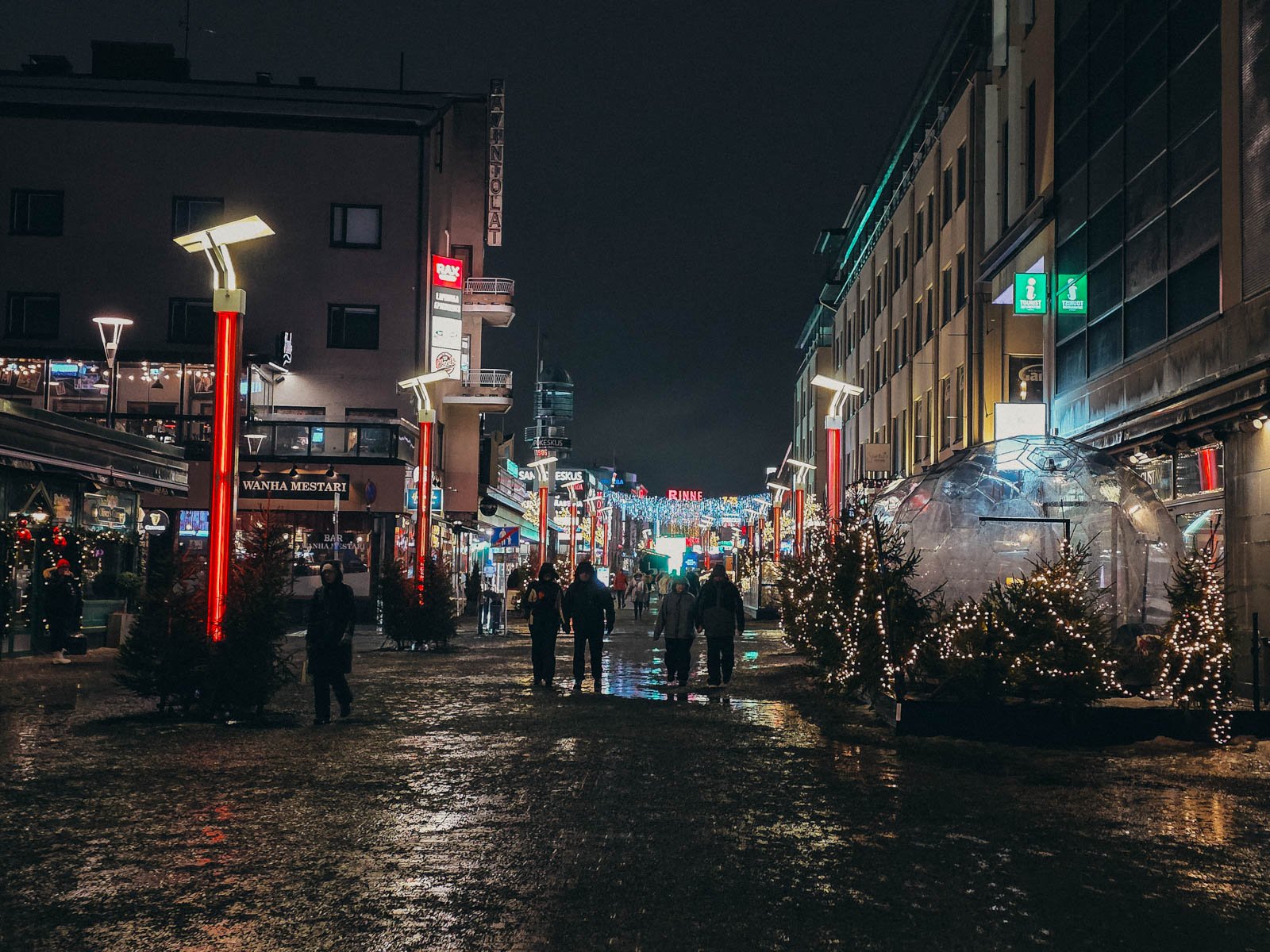 A lit up street at night with many bars and restaurants lining the street and colourful Christmas lights in Rovaniemi