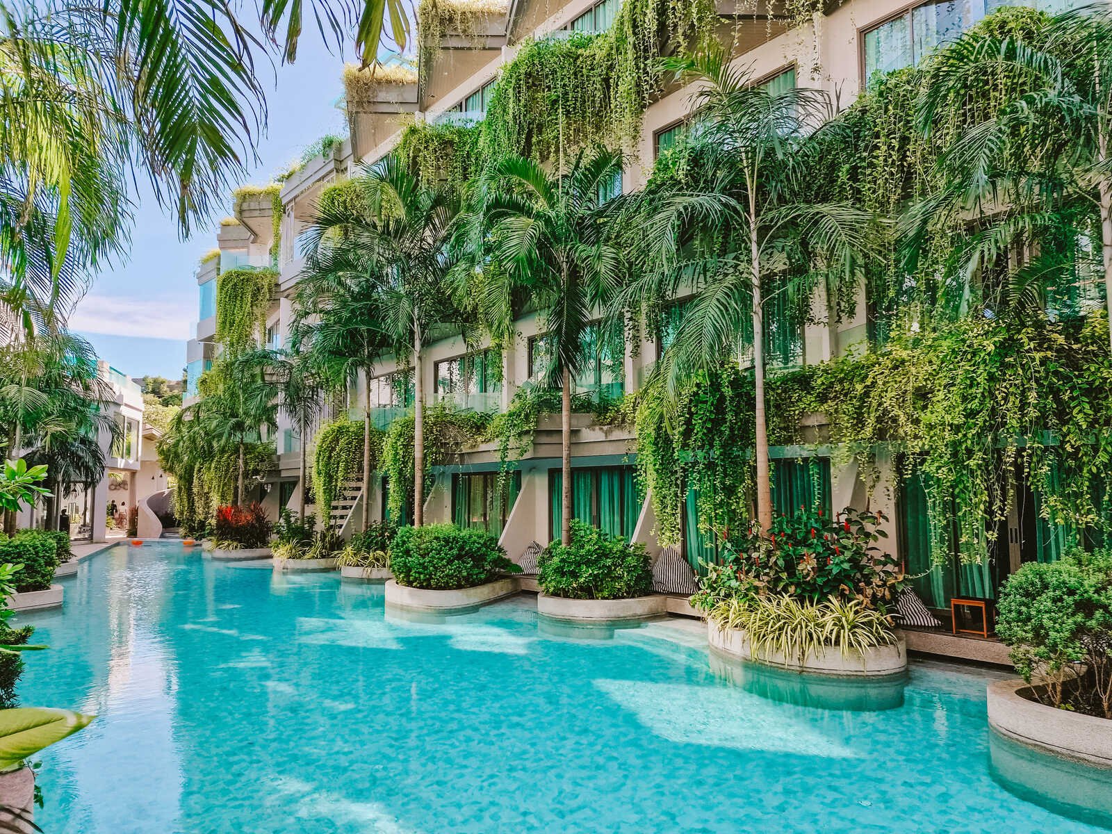 a hotel pool lined with pool access rooms with lots of palm trees and vines hanging on the hotel