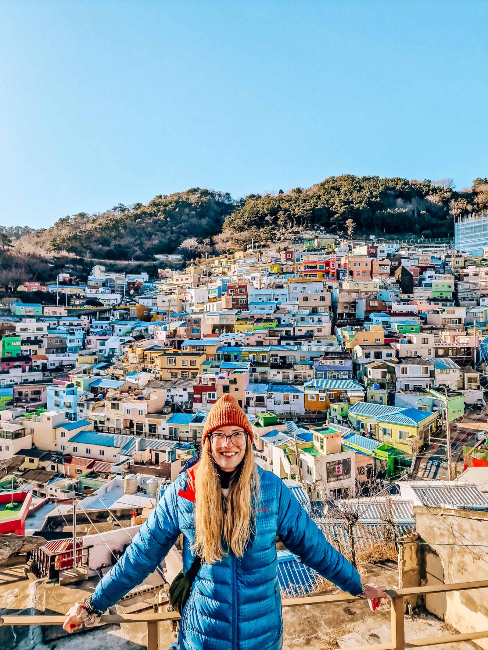 Helena standing on a balcony with a whole colourful village of hundreds of houses on the hillside behind her