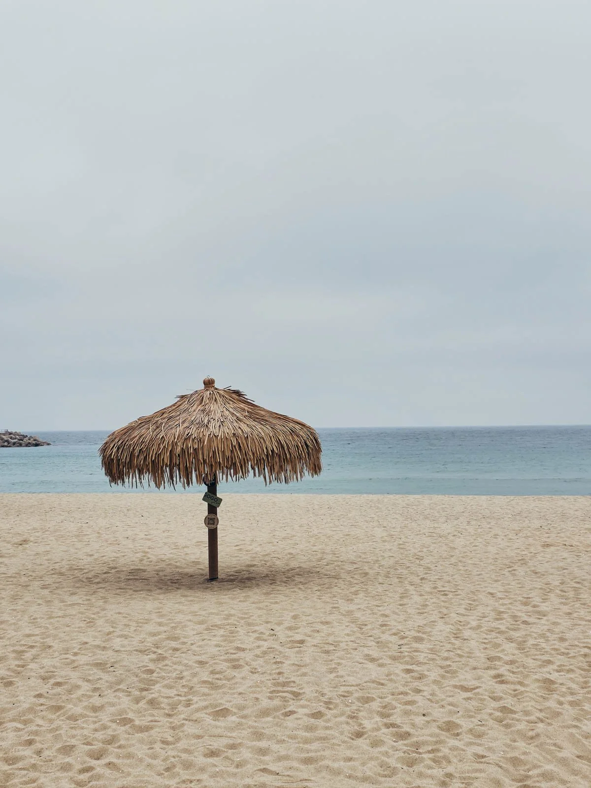 A sandy beach with the sea beyond and a single parasol in the sand