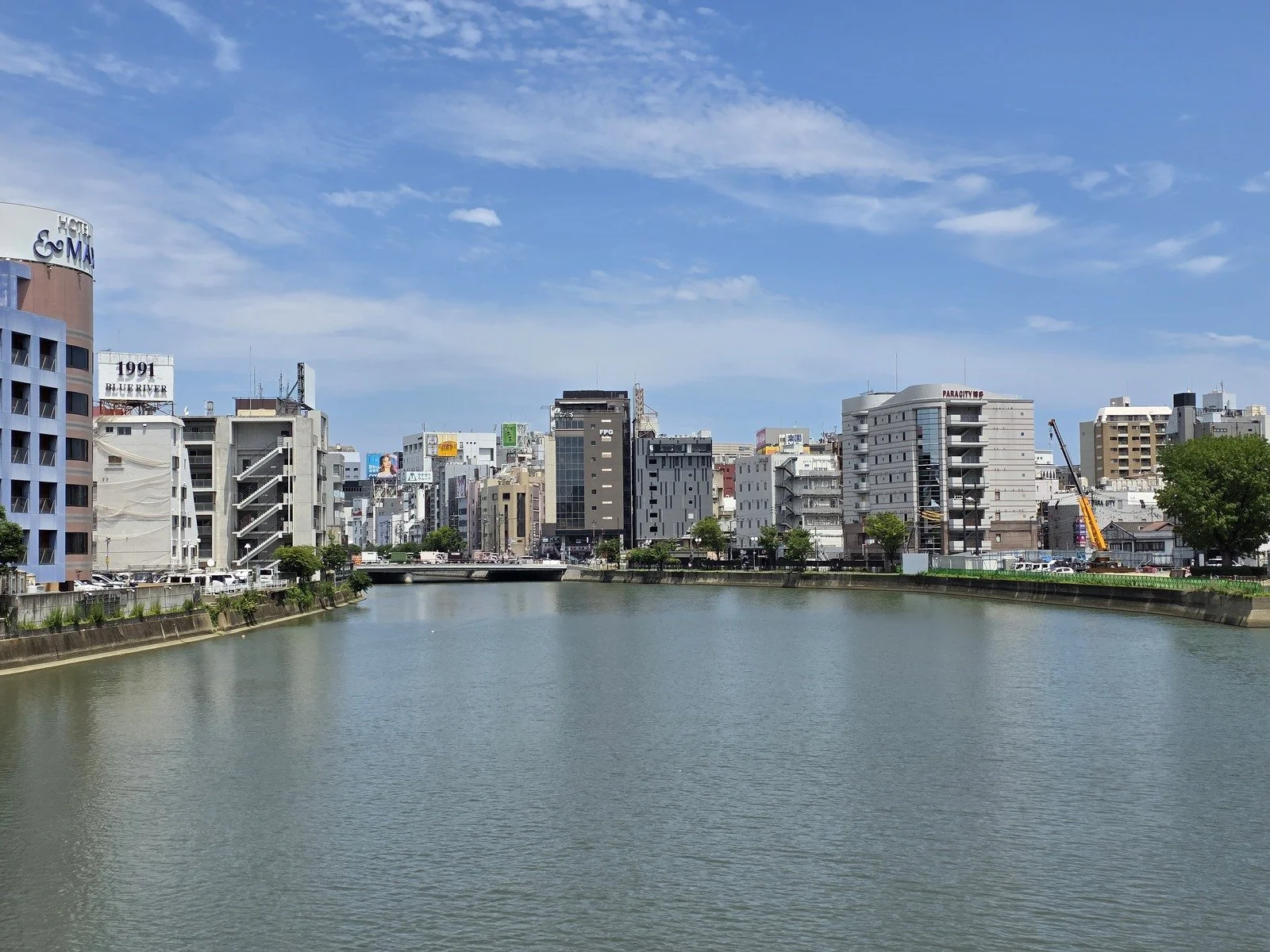 a river on a sunny day with blue sky and various city buildings lining each side of the river