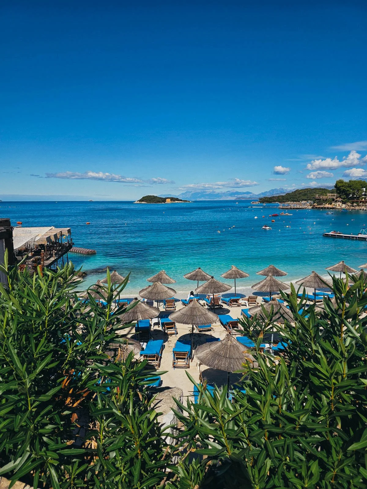 A white sand beach on the Albanian Riviera in Ksamil with clear blue and turquoise water. On the beach are many beach chairs and umbrellas