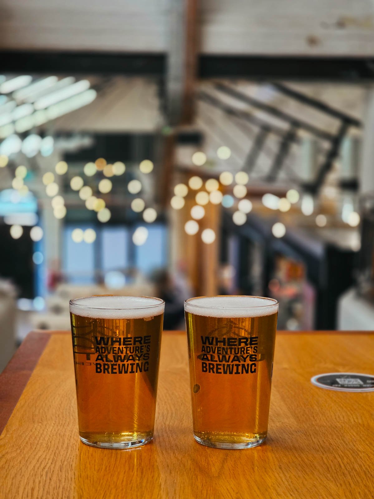 Two pints of beer on a table with the blurred background of a food hall with fairylights in the background