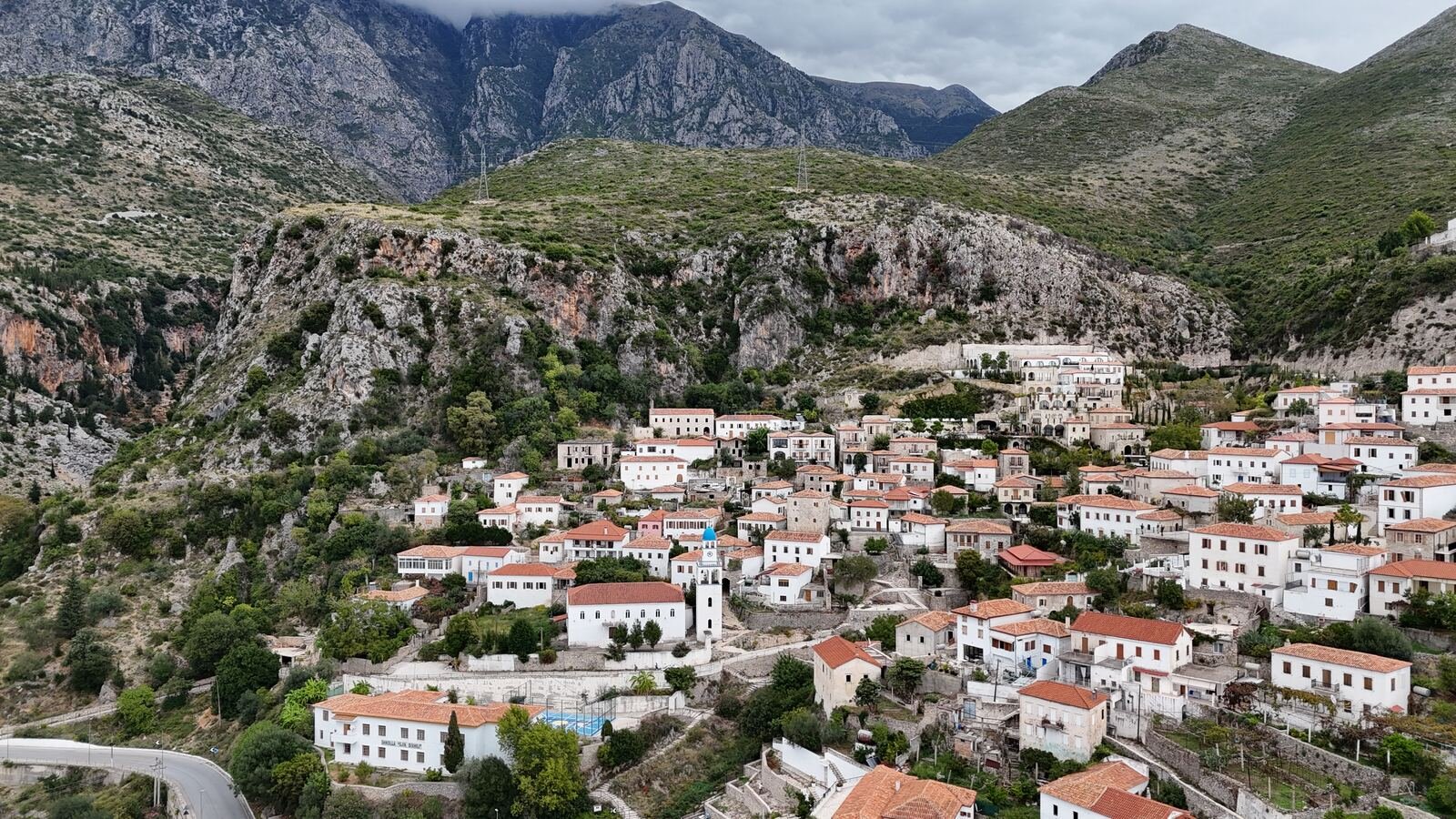 a town built on the hillside with white washed buildings and terracotta rooftops, a rocky mountain is behind