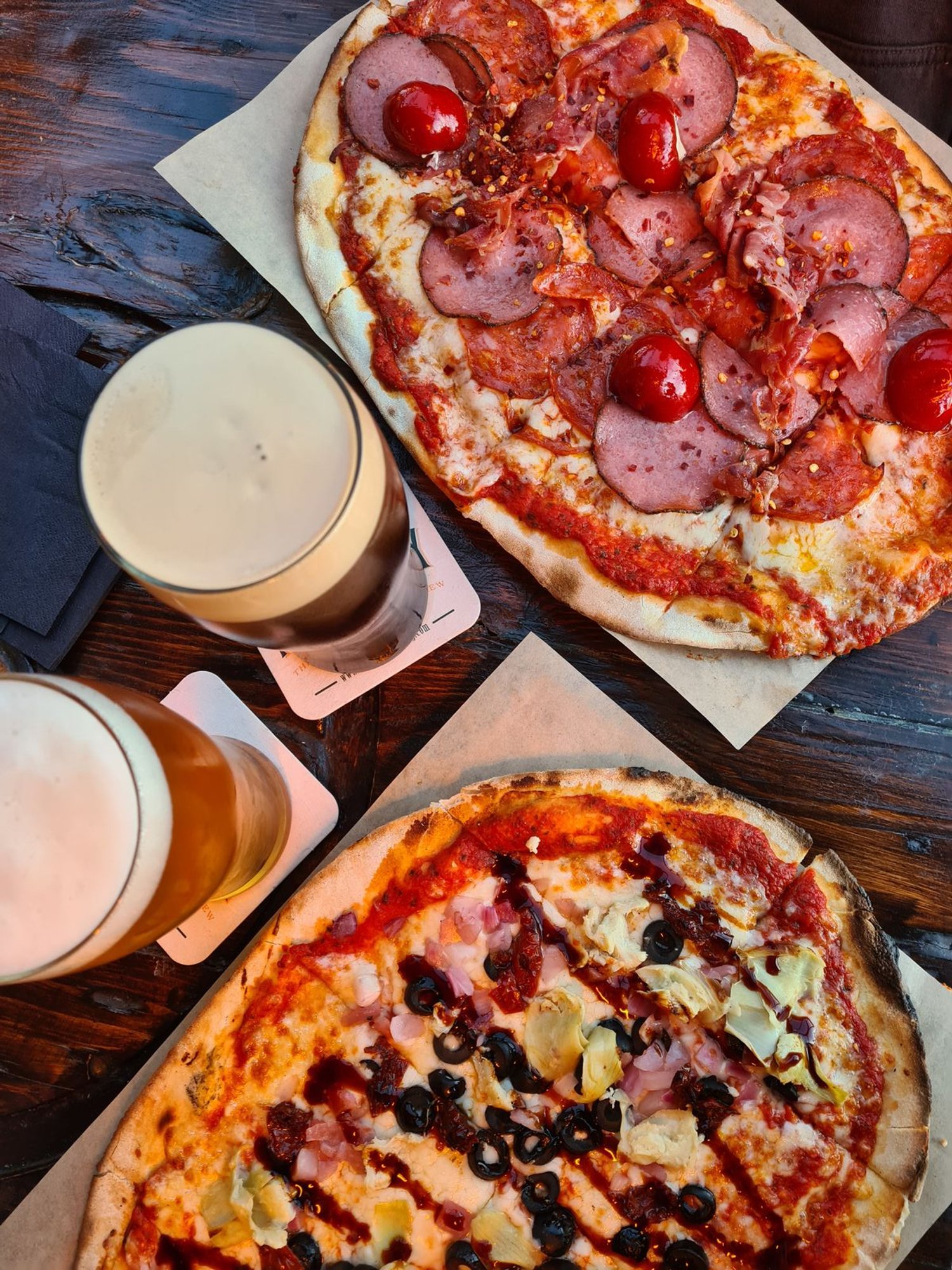 two large stonebaked pizzas with two pints of beer on a table