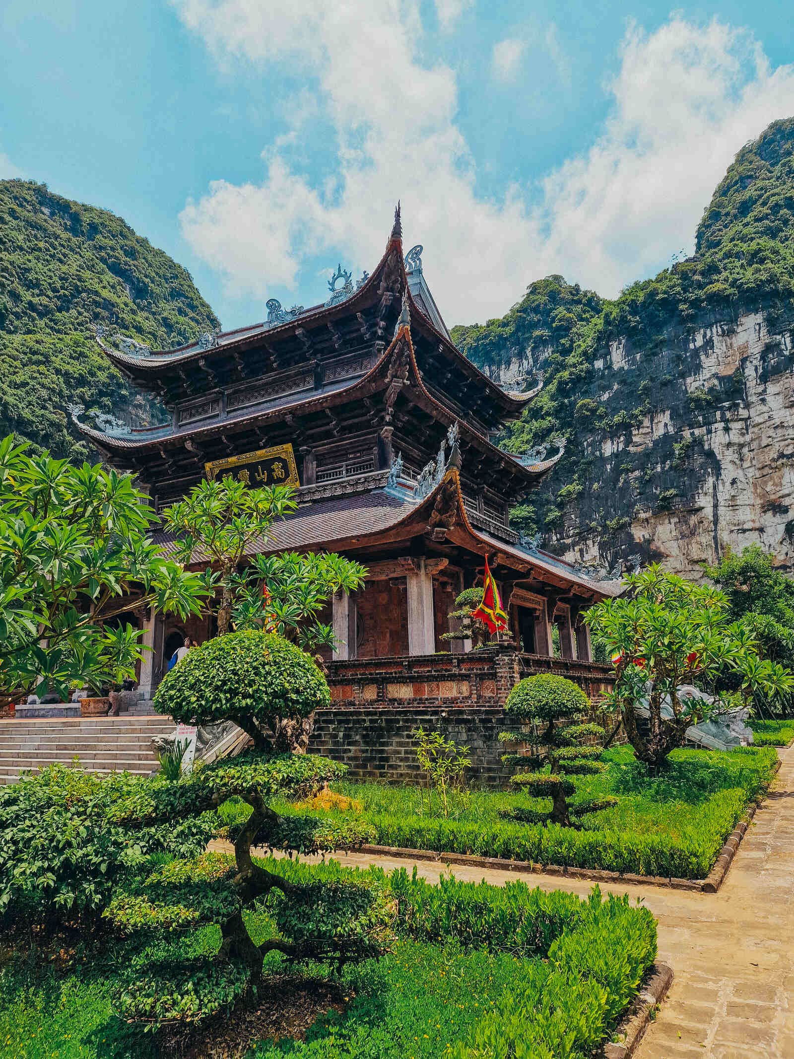 a three tier wooden temple pagoda surrounded by greenery and cliffs