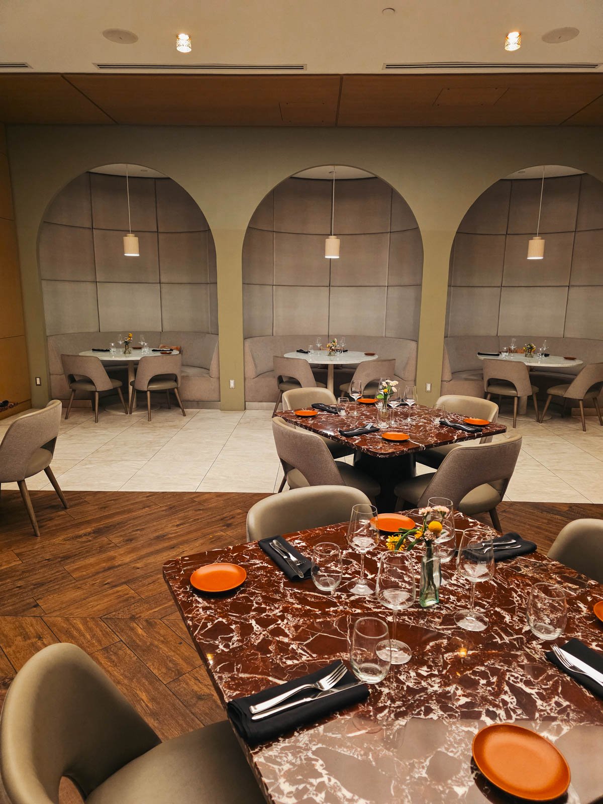 The interior of a restaurant with booth seating and tables in the centre set up with cutlery and glassware