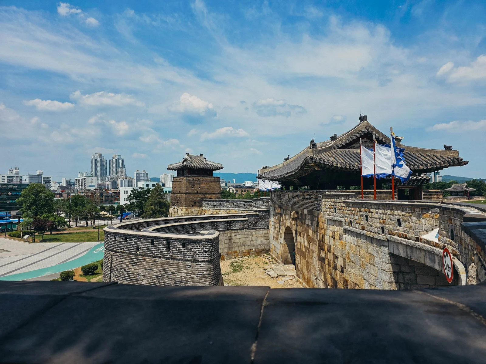 A large old stone fortress with ornate roofs. You cans see many large modern city buildings in the distance