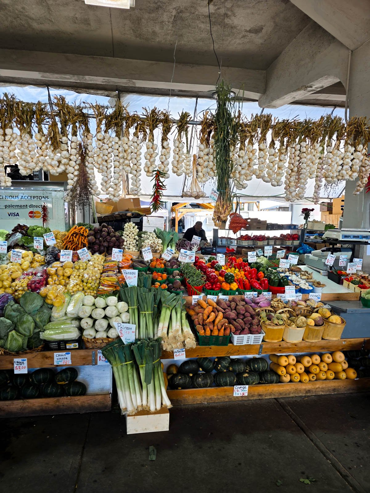 A market stand full of fresh and colourful vegetables with bunches of garlic hanging down from the top
