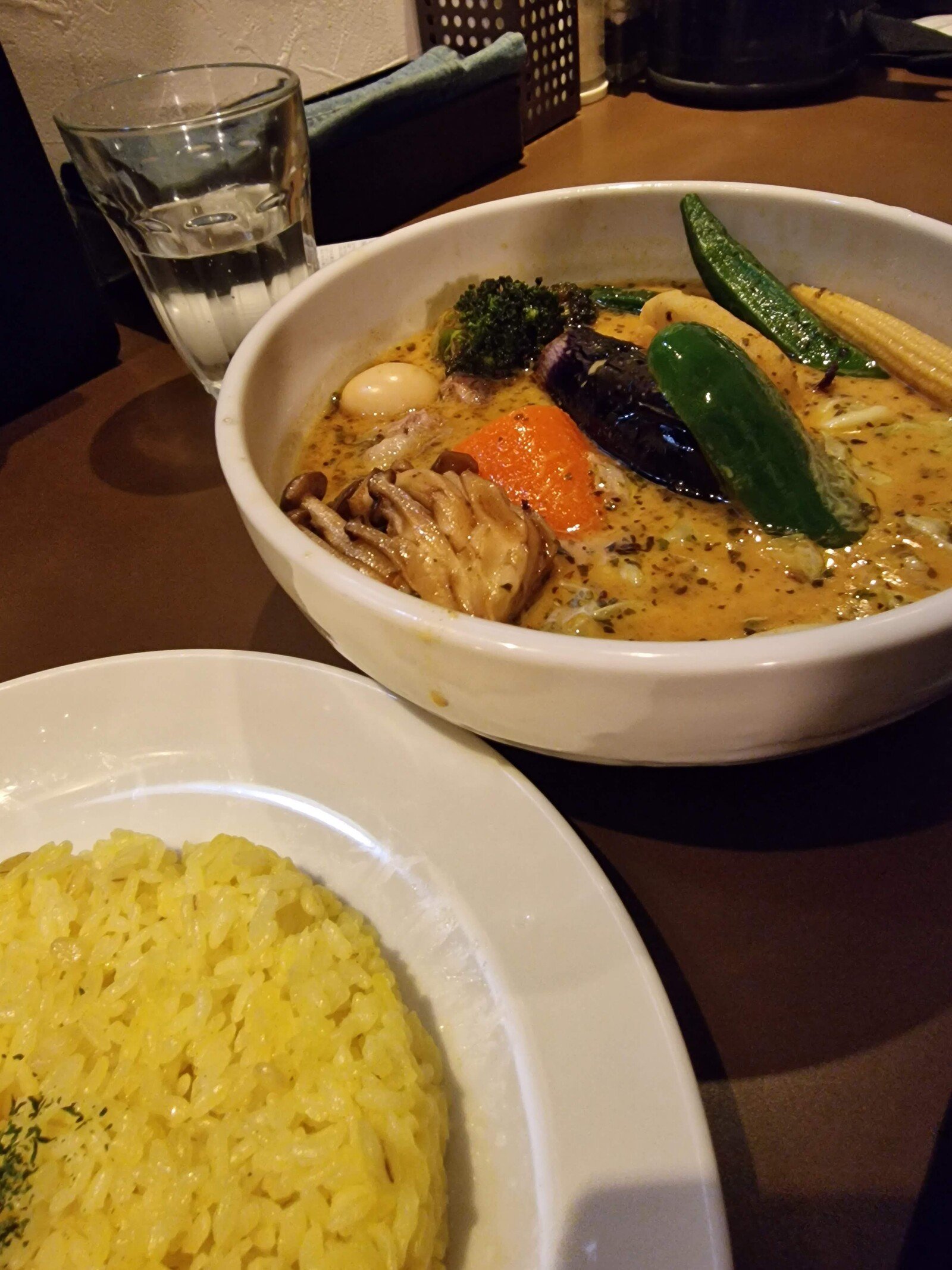 a bowl of yellow soup broth with vegetables in it and a plate of yellow rice next to it - Hokkaido soup curry