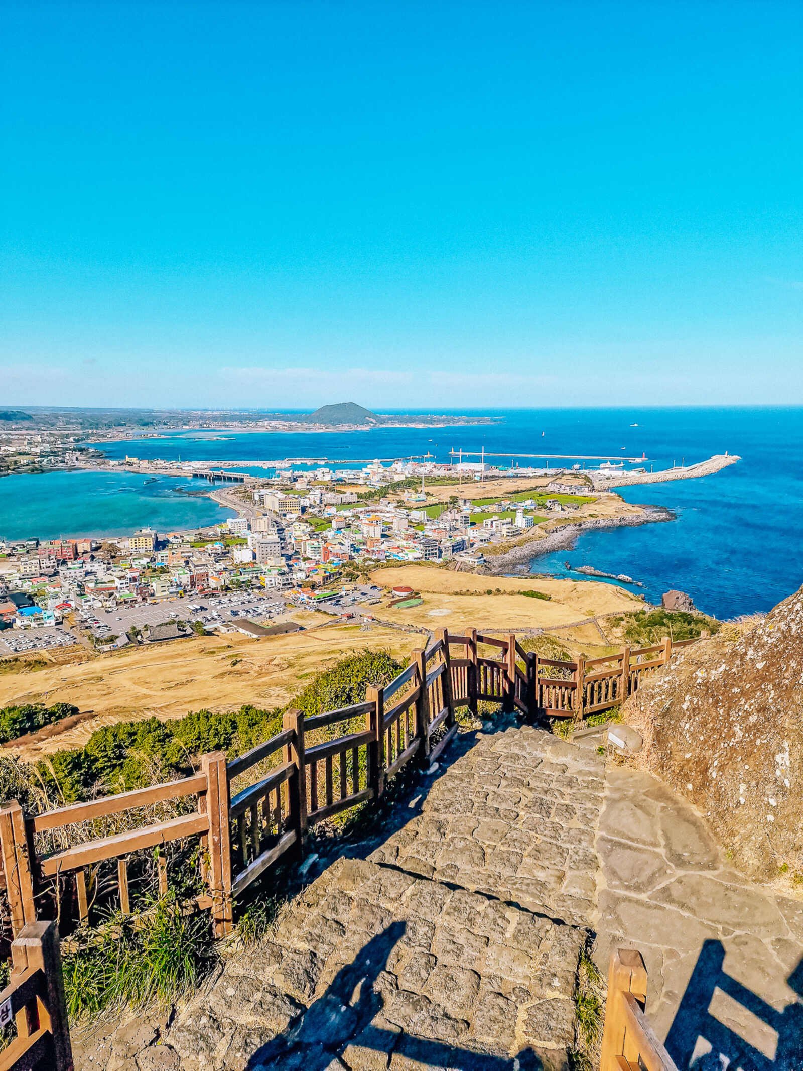 Looking down stone steps to a view of a small coastal town surrounded by blue sea