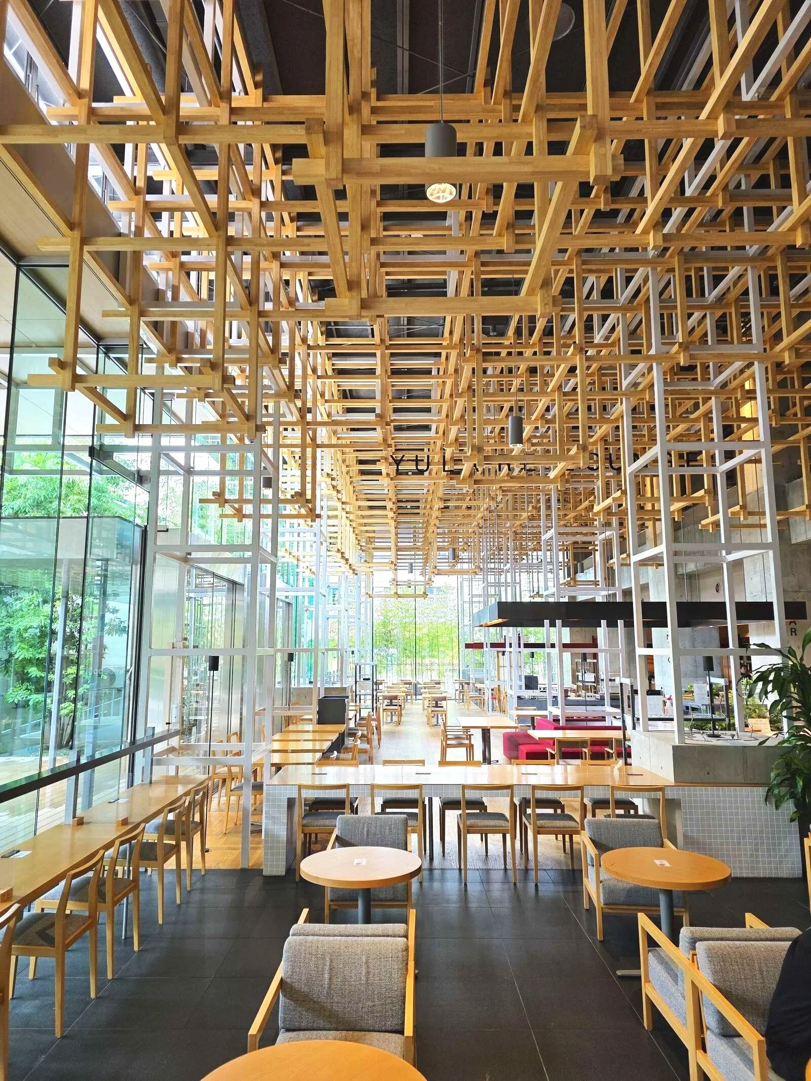 a hotel lobby with intricate wooden pieces hanging across the whole ceiling and many tables and chairs inside a well-lit room with floor to ceiling glass walls in Beppu