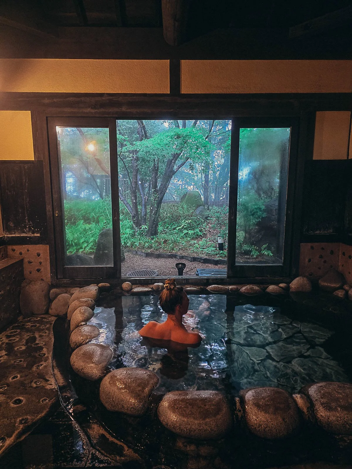 Helena a small pool in an onsen which is surrounded by stones and has a open doorway which looks out onto a small private garden