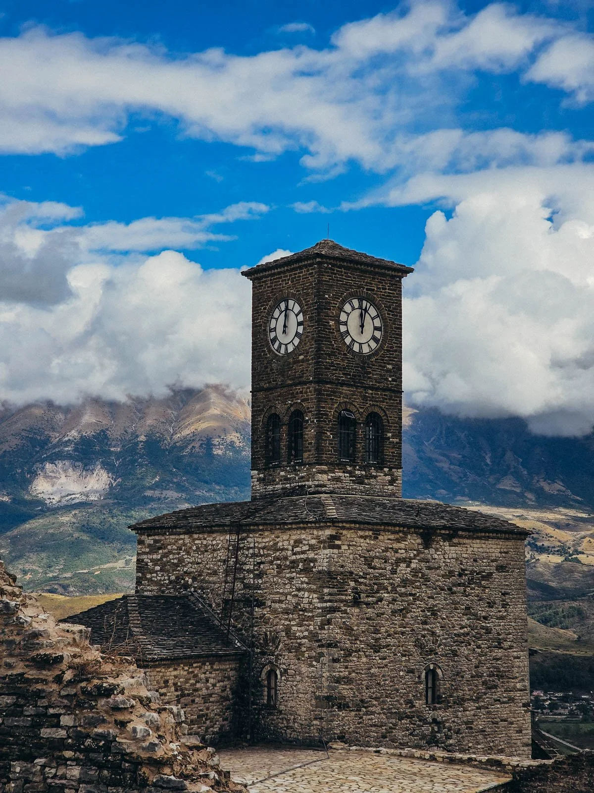 An old stone clock tower with a mountain range in the background