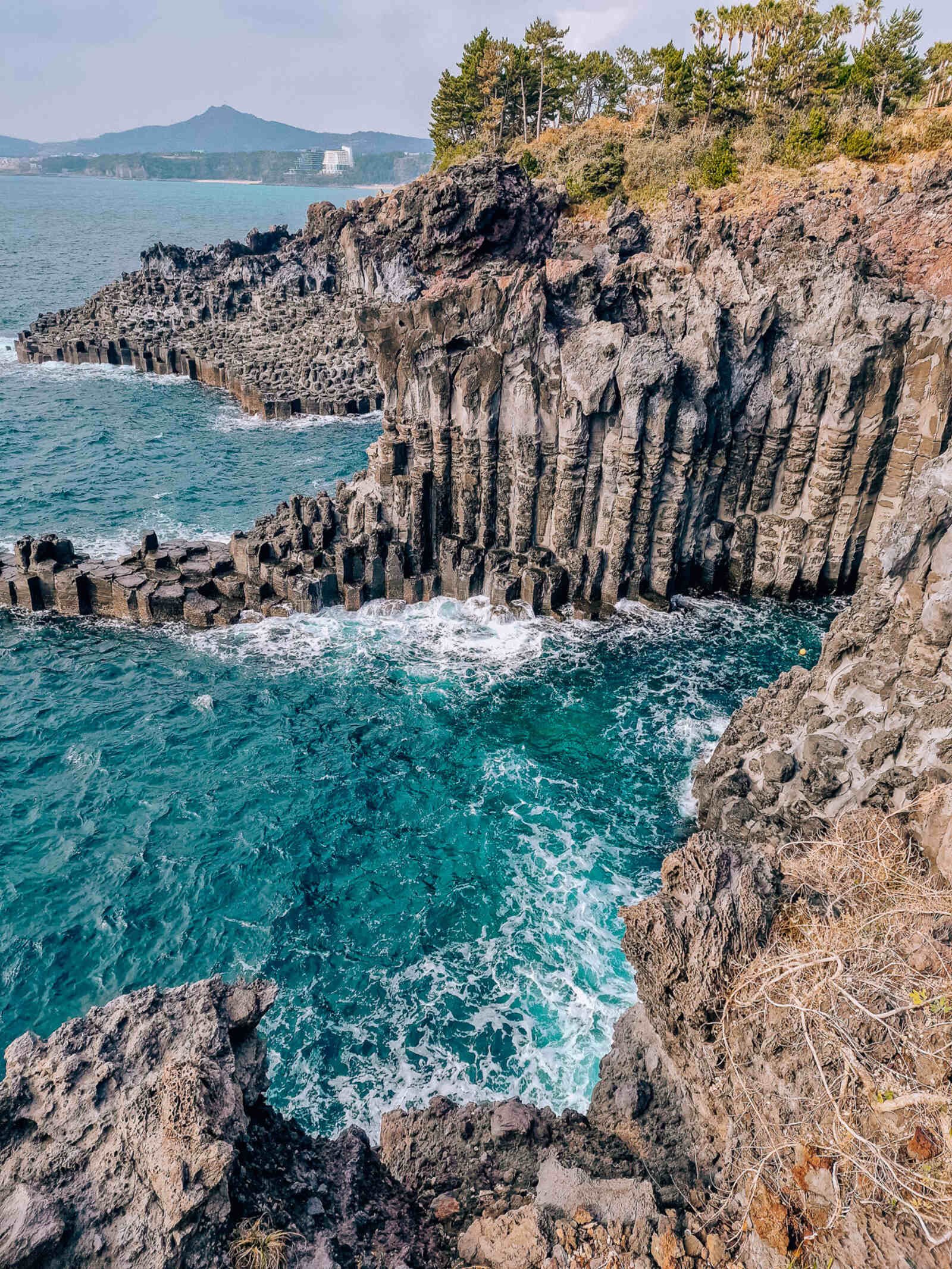 a coastal area with unique basalt columns forming the coastal rocks. The sea is teal blue