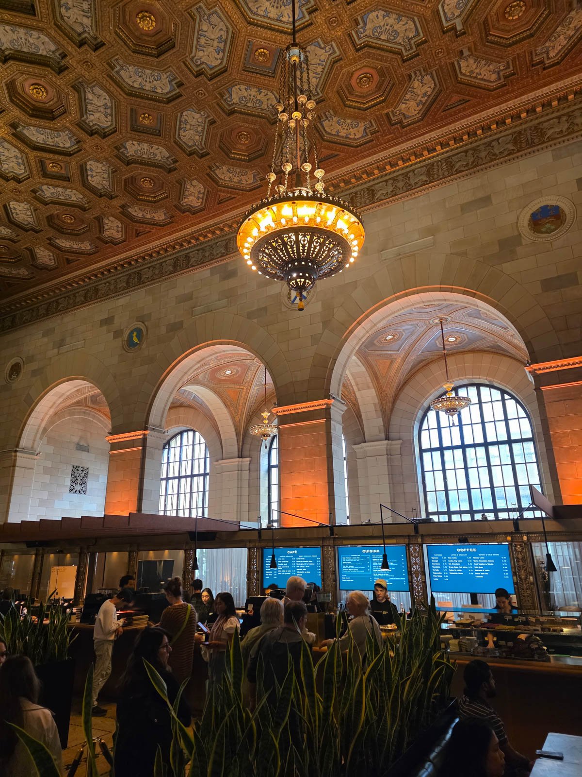 The interior of a stone building with intricate ceiling and a big chandelier inside a coffee shop in Montreal