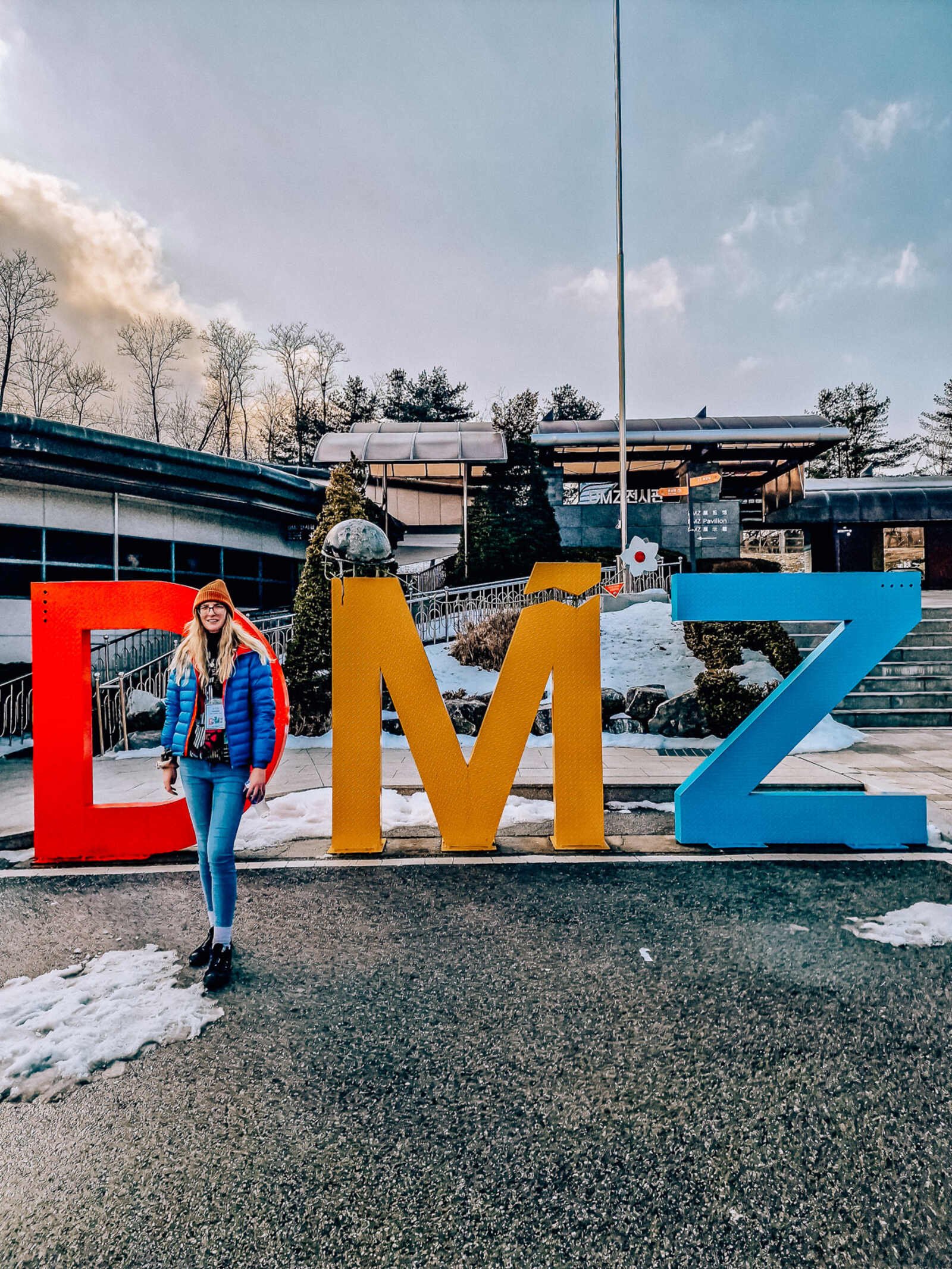 Woma standing in front of three freestanding letters in red, yellow and blue that read DMZ