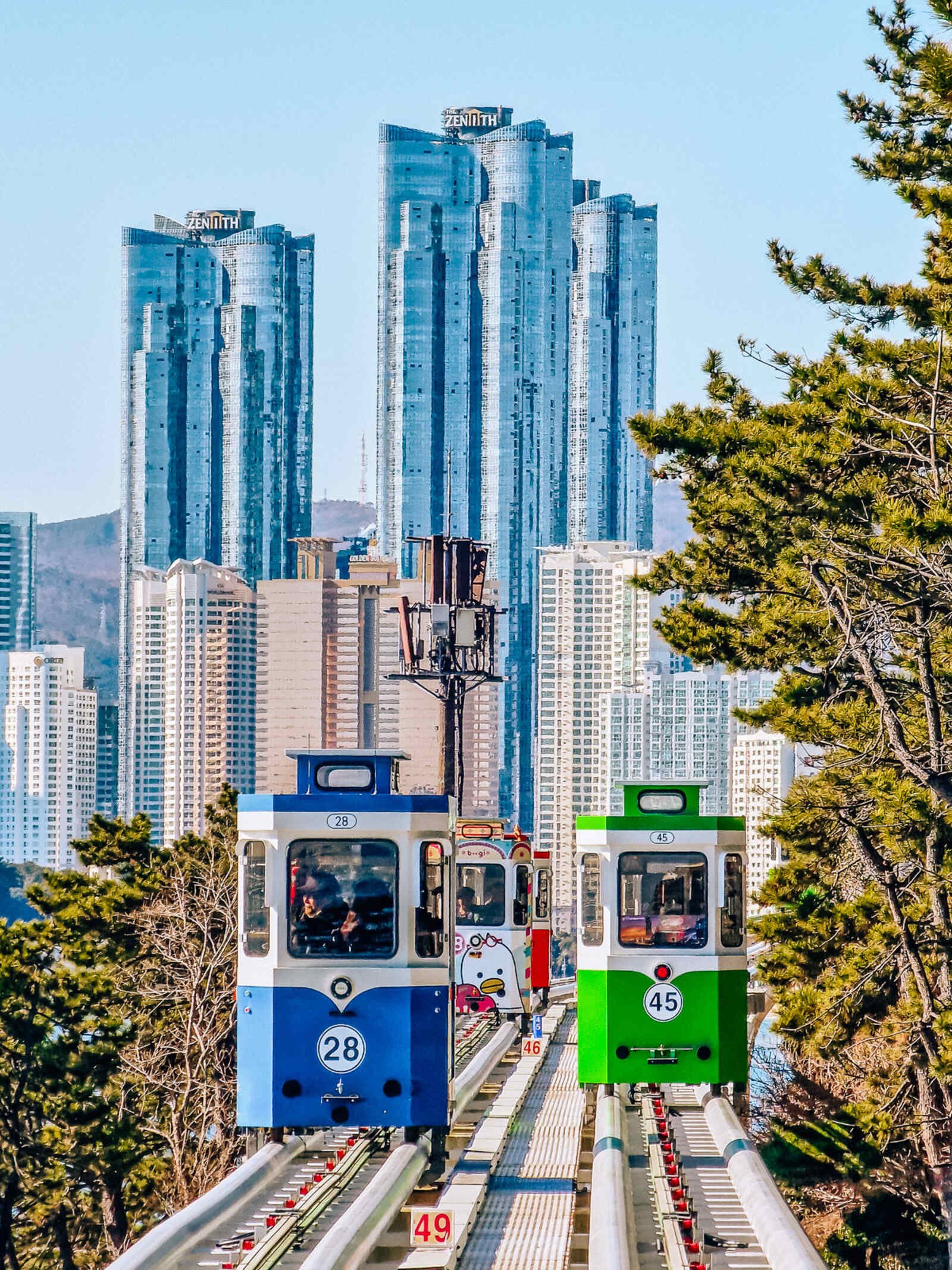 four sky capsules on the track with skyscrapers looming behind