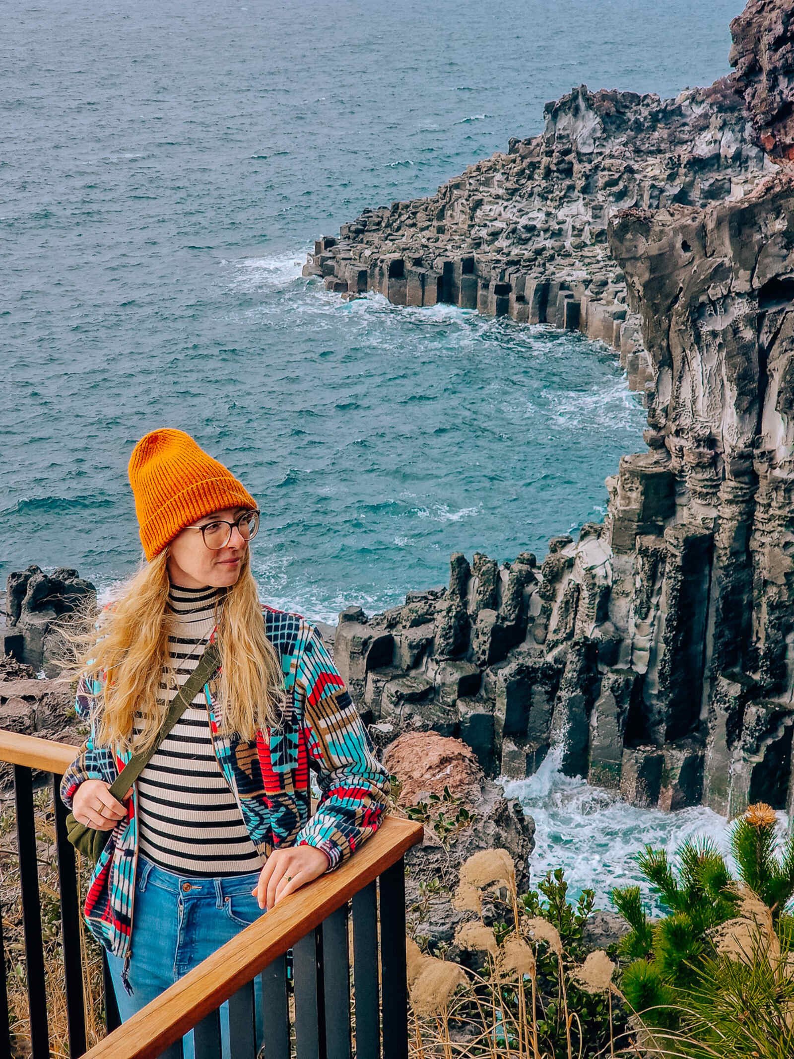 a woman on an observation deck looking down on a coastline of volcanic rock