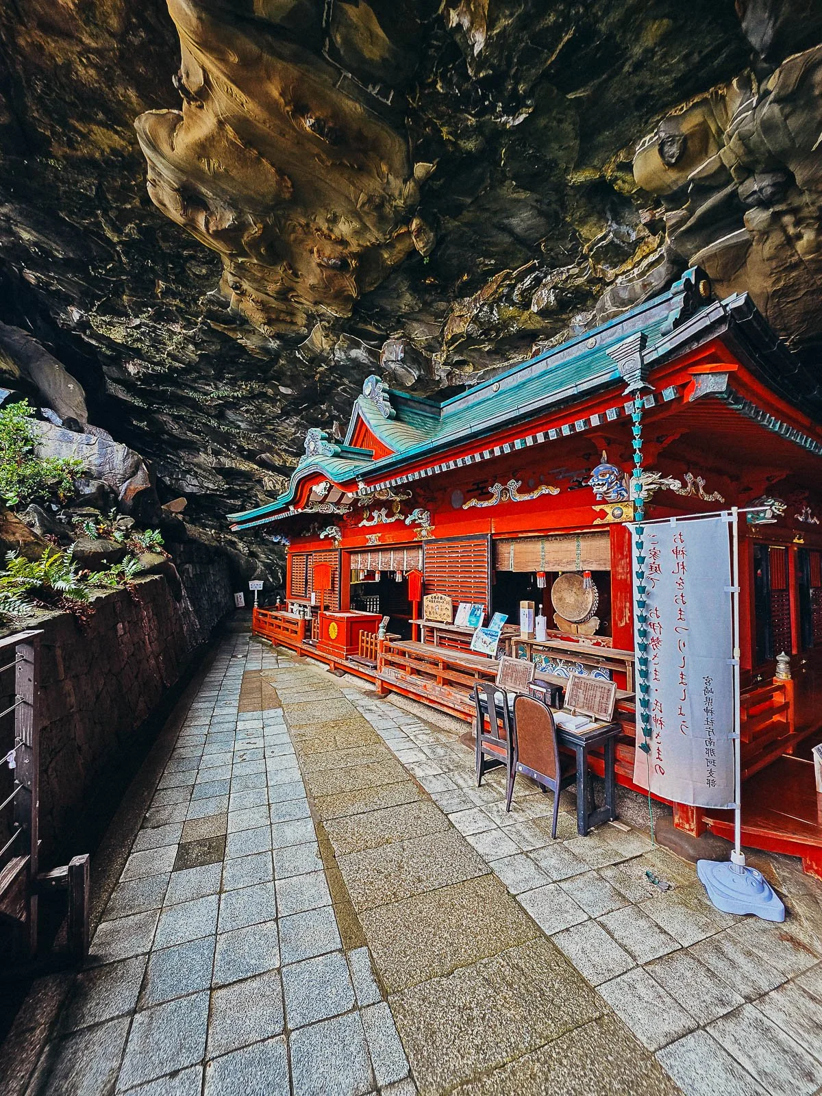 a red shinto shrine built inside a cave in Japan with the cave rock roof low over the top of the shrine