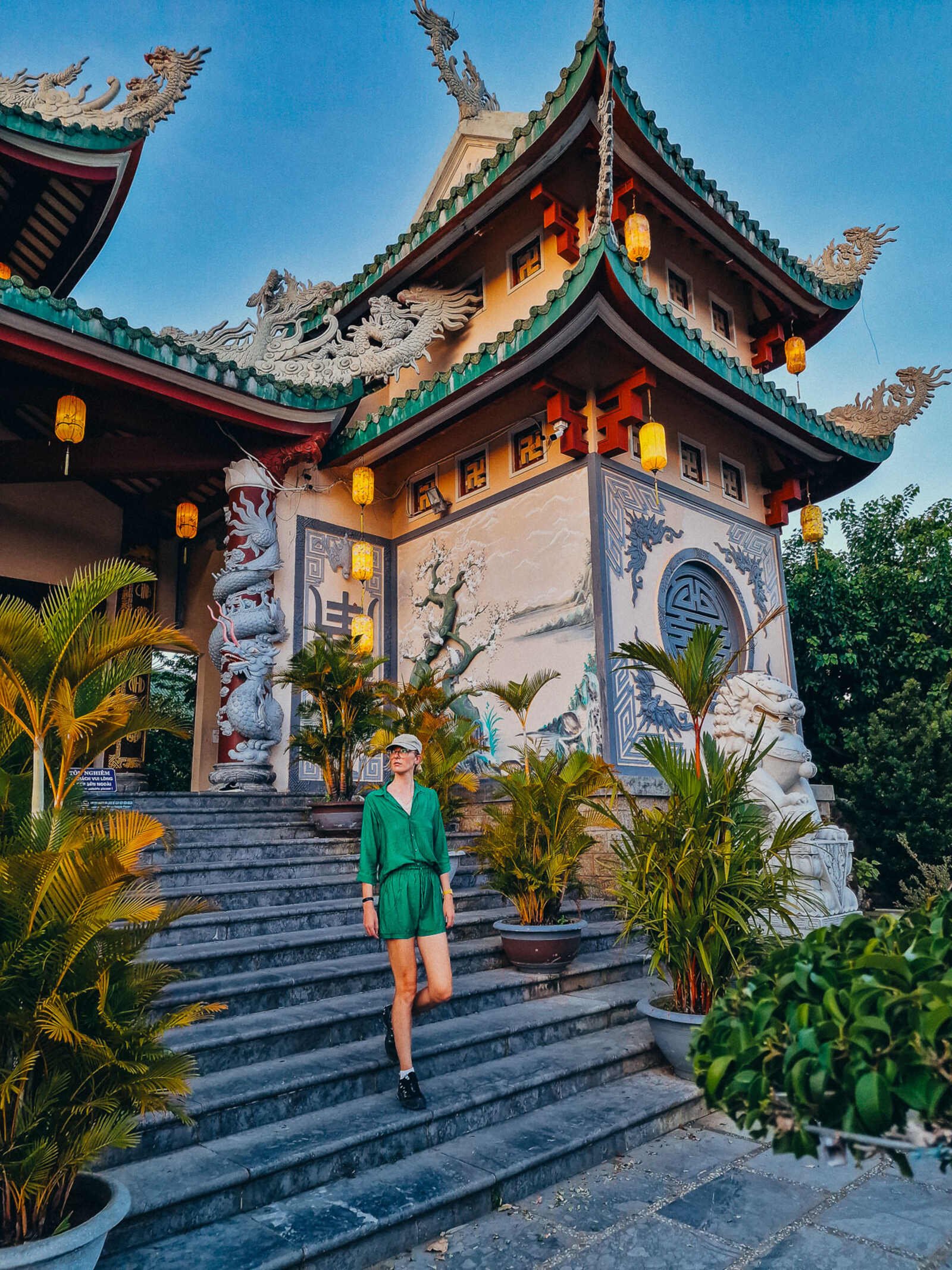 Helena in green on the stone steps of a ornate temple decorated in many dragon statues and paintings
