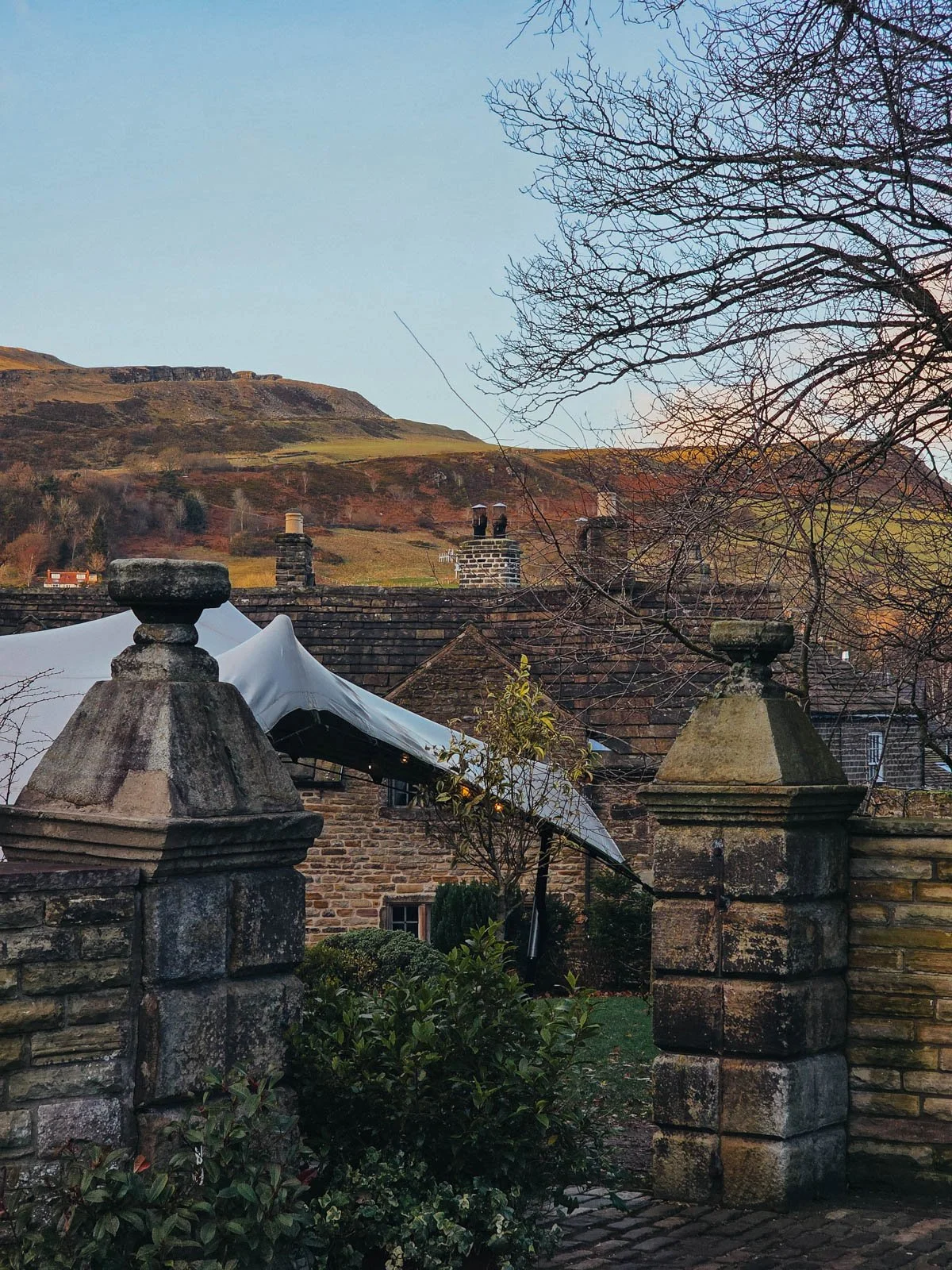 Two stone pillars with a stone house behind and a tall hill in the distance