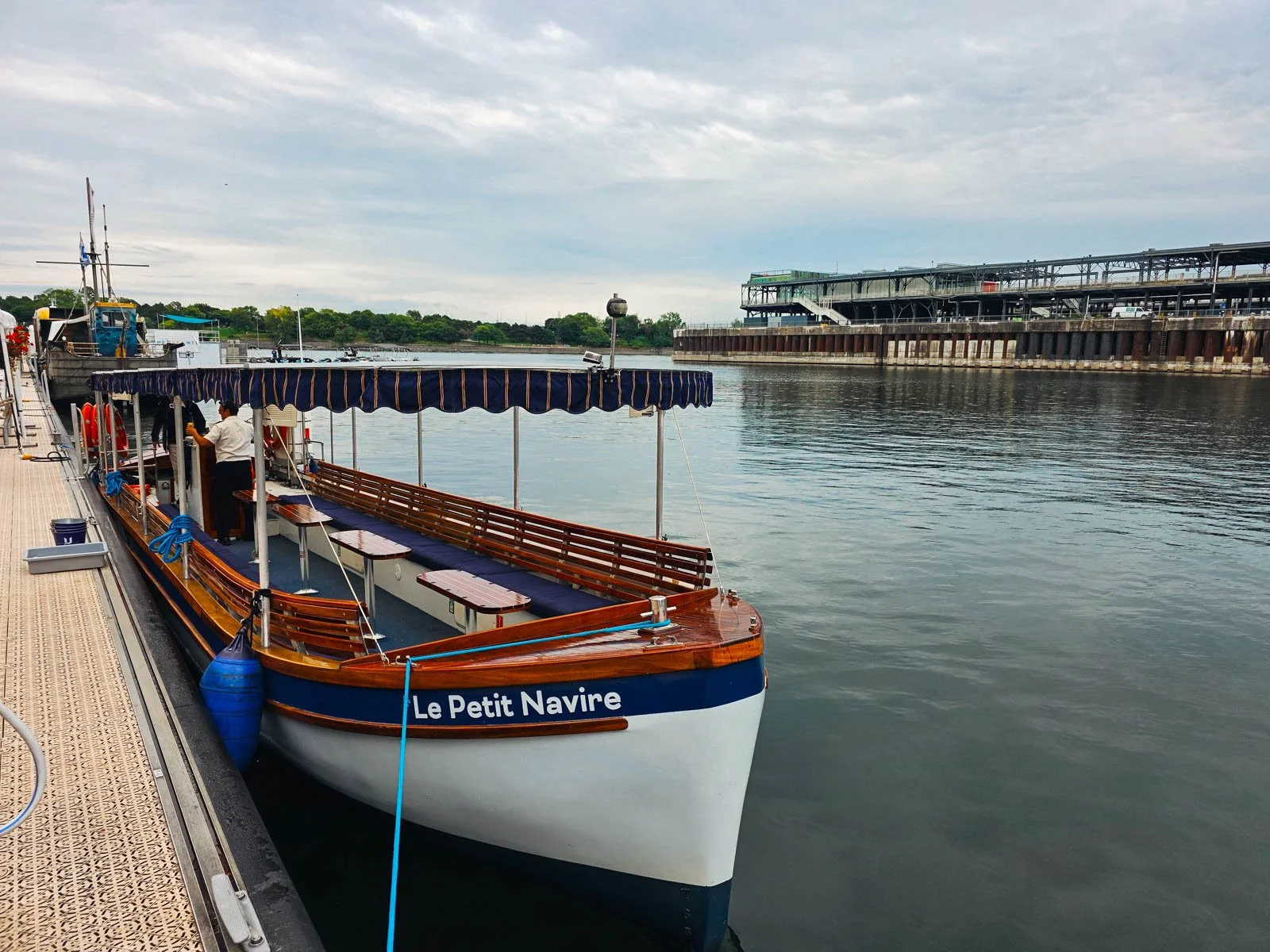 An old style wooden boat painted white and blue with a stripped canopy and seating along either side inside for visitors on a boat tour in Montreal