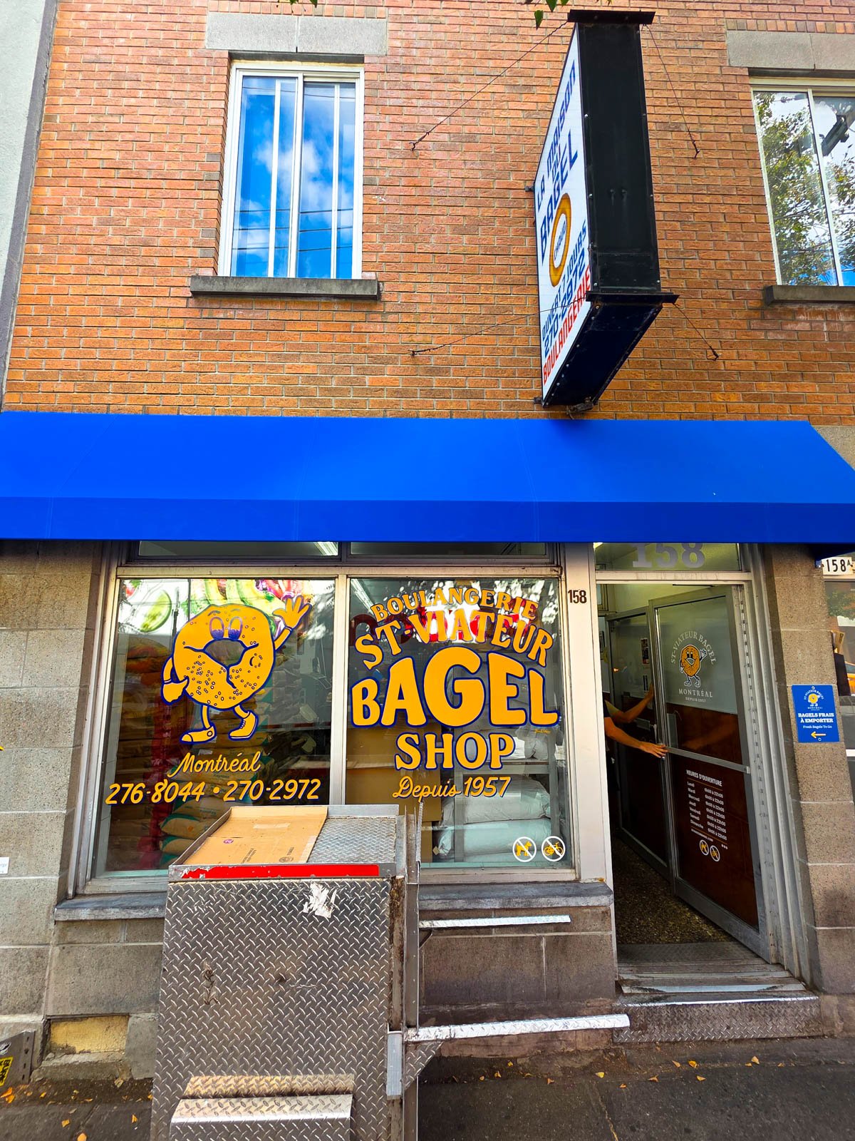 The front of a bagel shop with blue awning and the window sign says "St Viateur Bagel Shop"