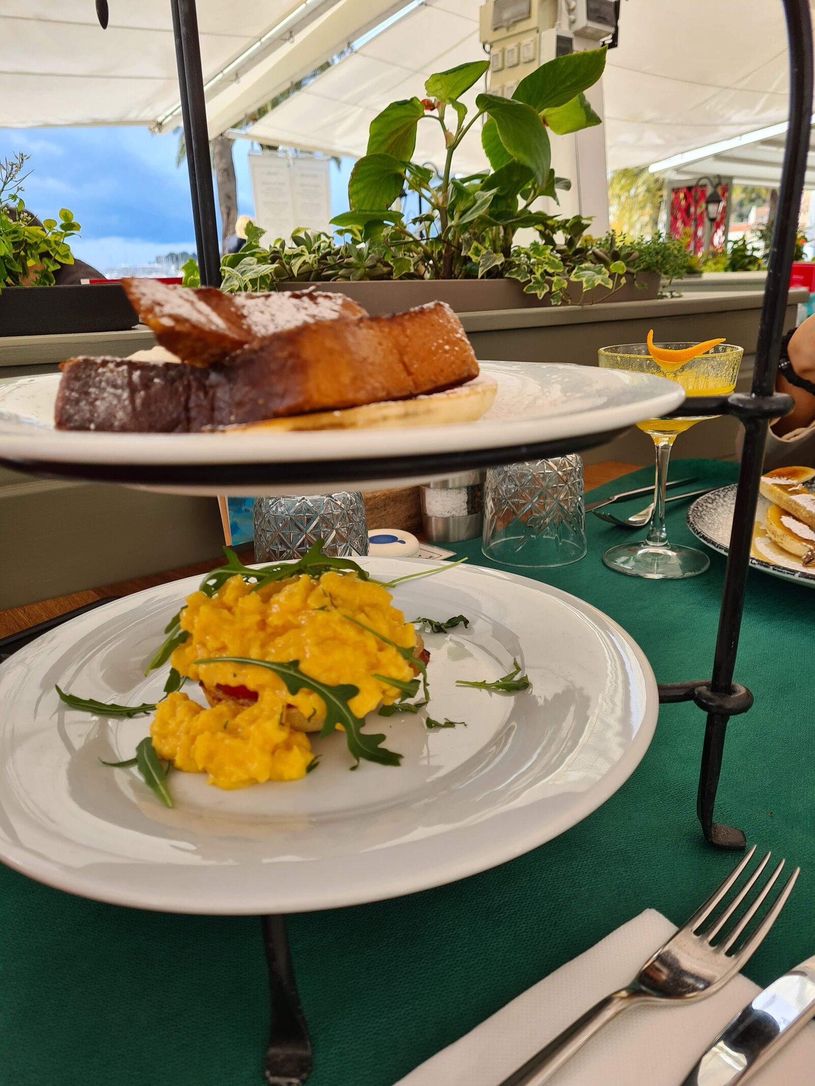 Two plates with brown French toast and a yellow egged dish stacked on a two tier fixture sitting on a table outside