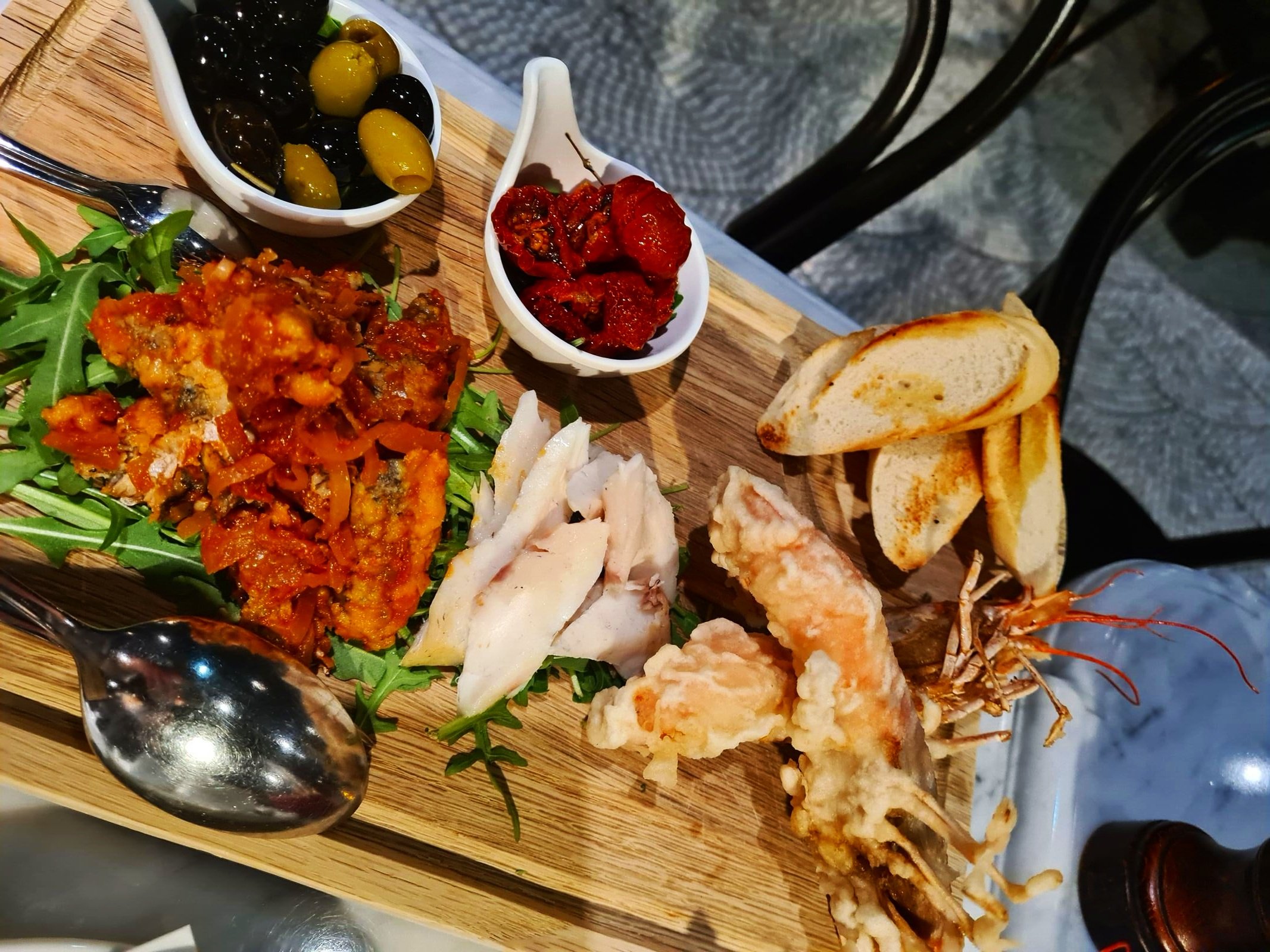 a food plater with olives, chorizo, fried prawns, white fish and salad
