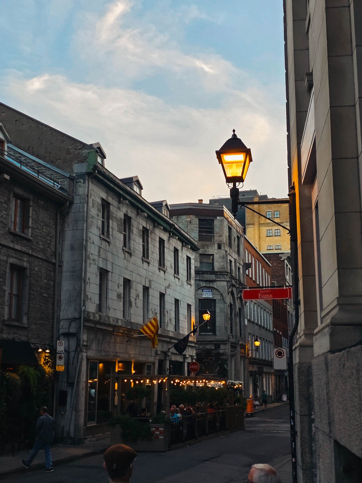 A cobbled street lined with stone buildings and warmly lit street lamps at dusk - visiting Old Montreal is one of the best things to do in Montréal