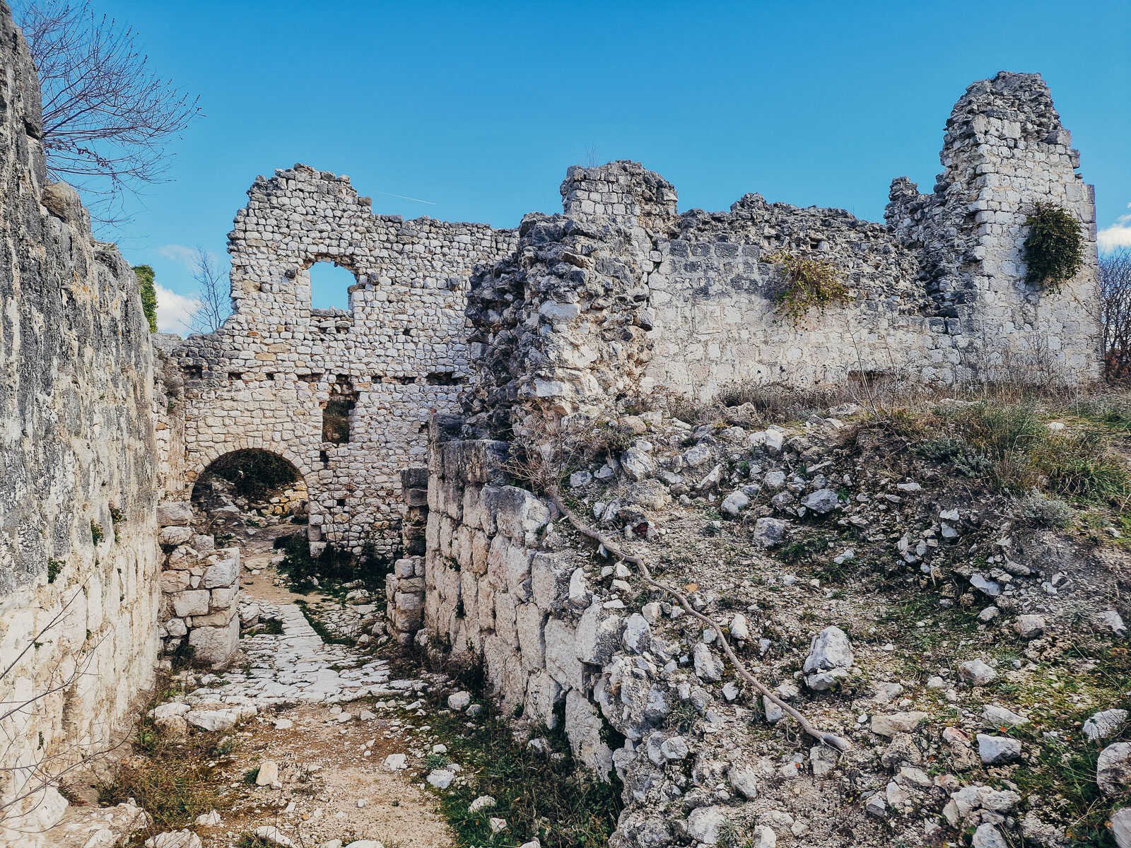 Stone ruins on an old fortress, the stones are white and grass grows in between, the sky is blue through holes where windows used to be, Vrana fortress in Croatia