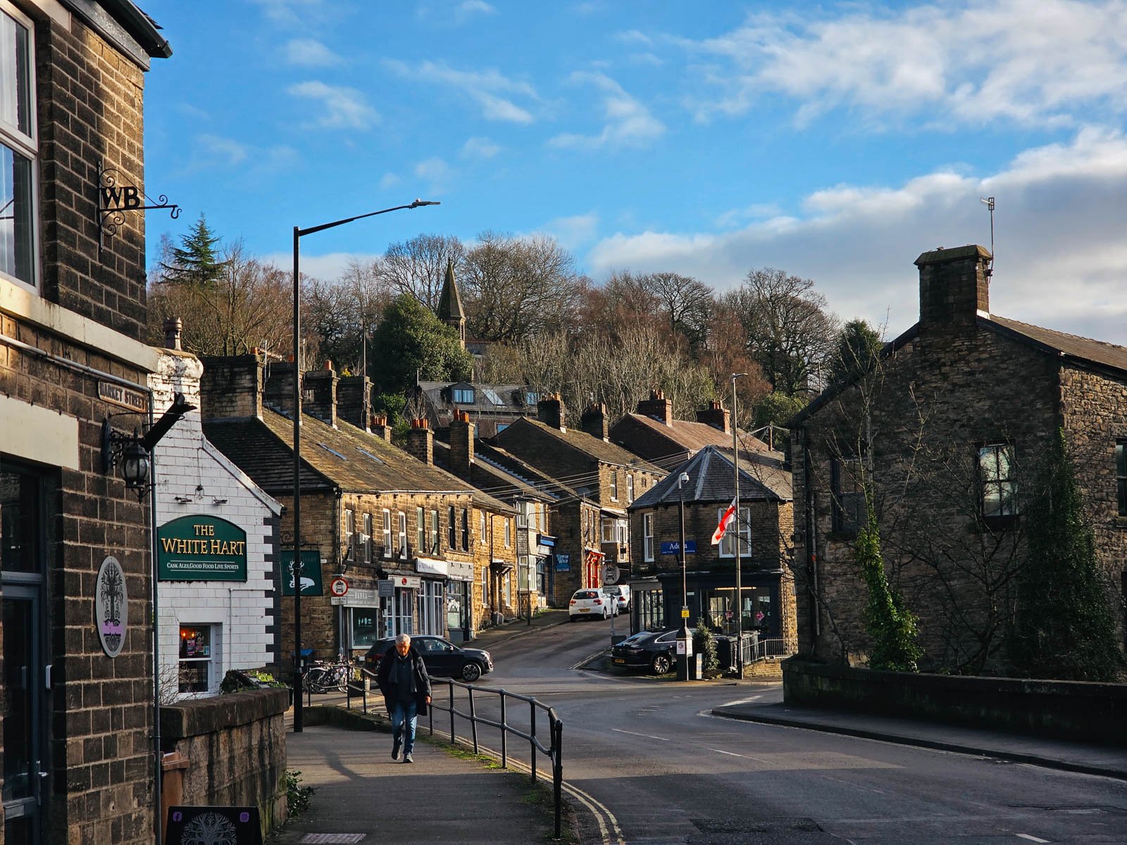 Looking down the street of a village in High peak, Peak Districtt with many stone terraced houses up a gradual hill and a church spire visible behind