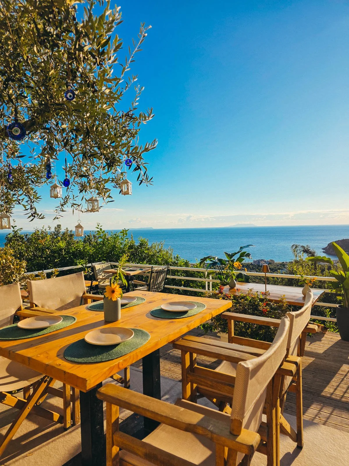 The wooden outside table and chairs of a restaurant with a view of the blue ocean in the far distance at a Himare hotel in Albania