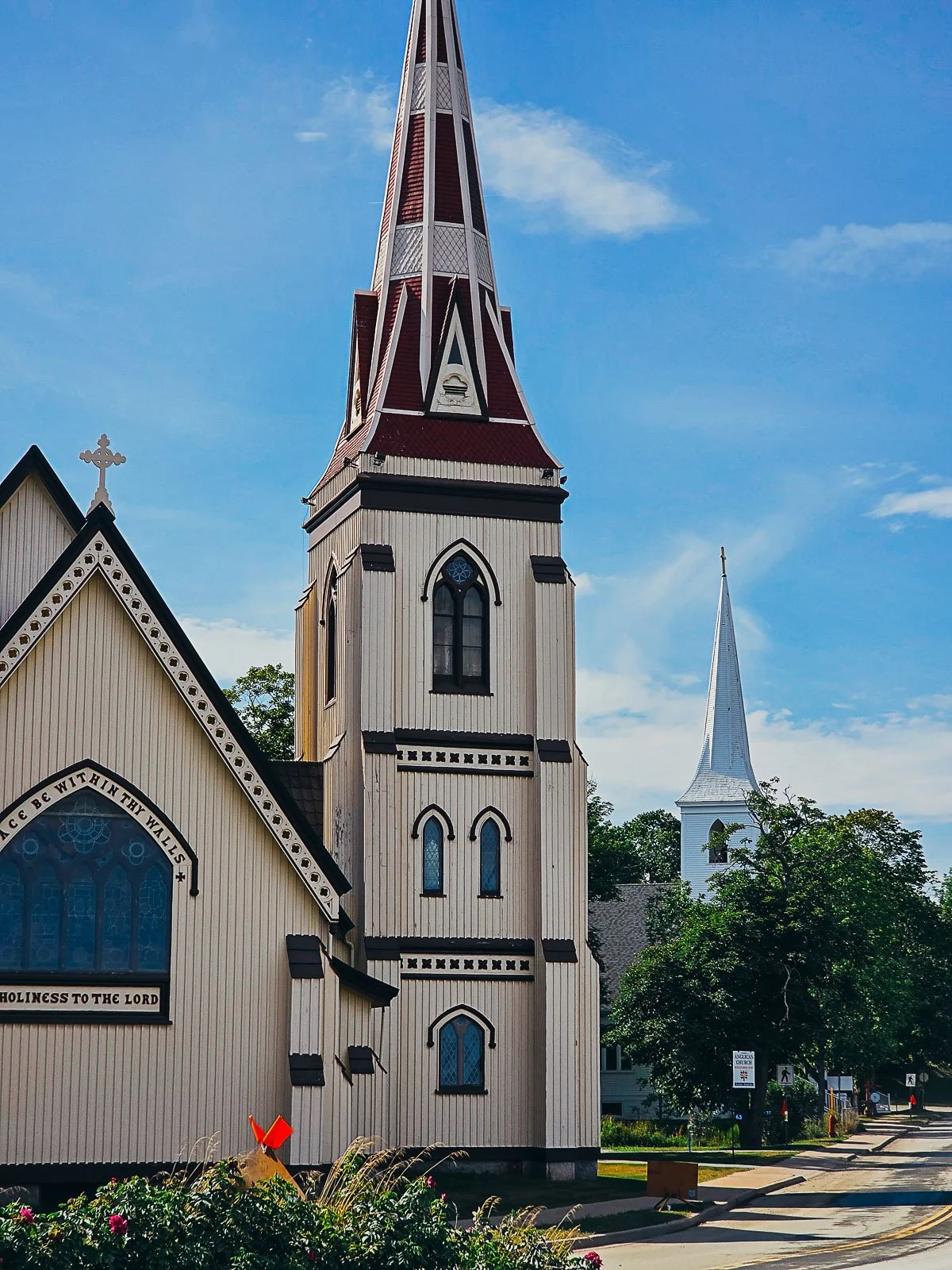 A light and dark brown church in the foreground with a spire and the spire of a white church visible in the distance beyond it