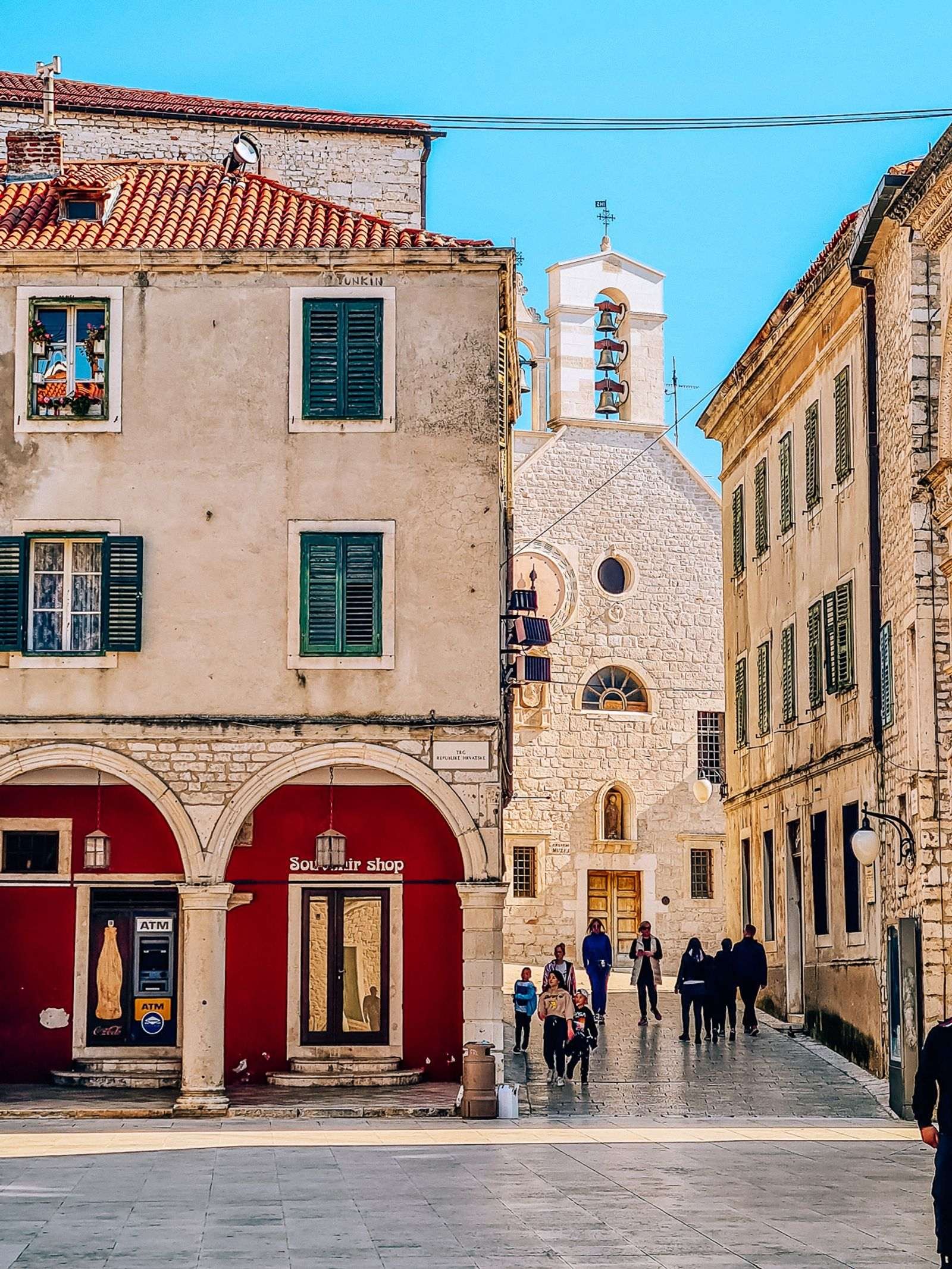 image in the town square o Sibenik with old stone buildings and a street down the righthand side with a church at the bottom