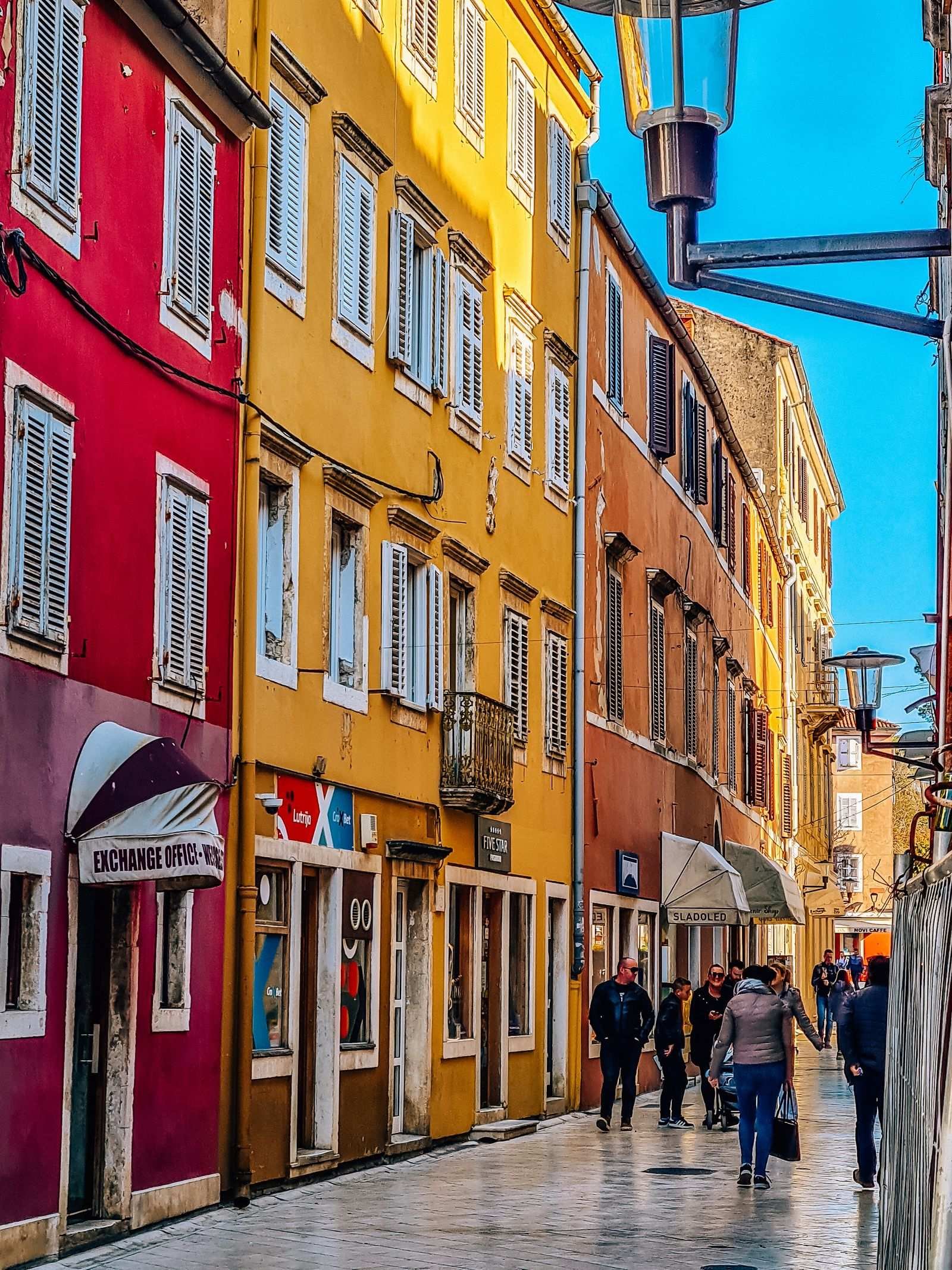 A colourful pedestrian street with people walking down on a sunny day, buildings are red, yellow and orange