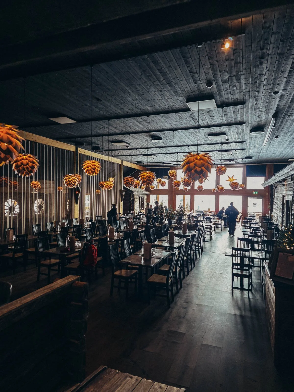 A large dark wooden hotel restaurant with lots of seating and large windows at the back
