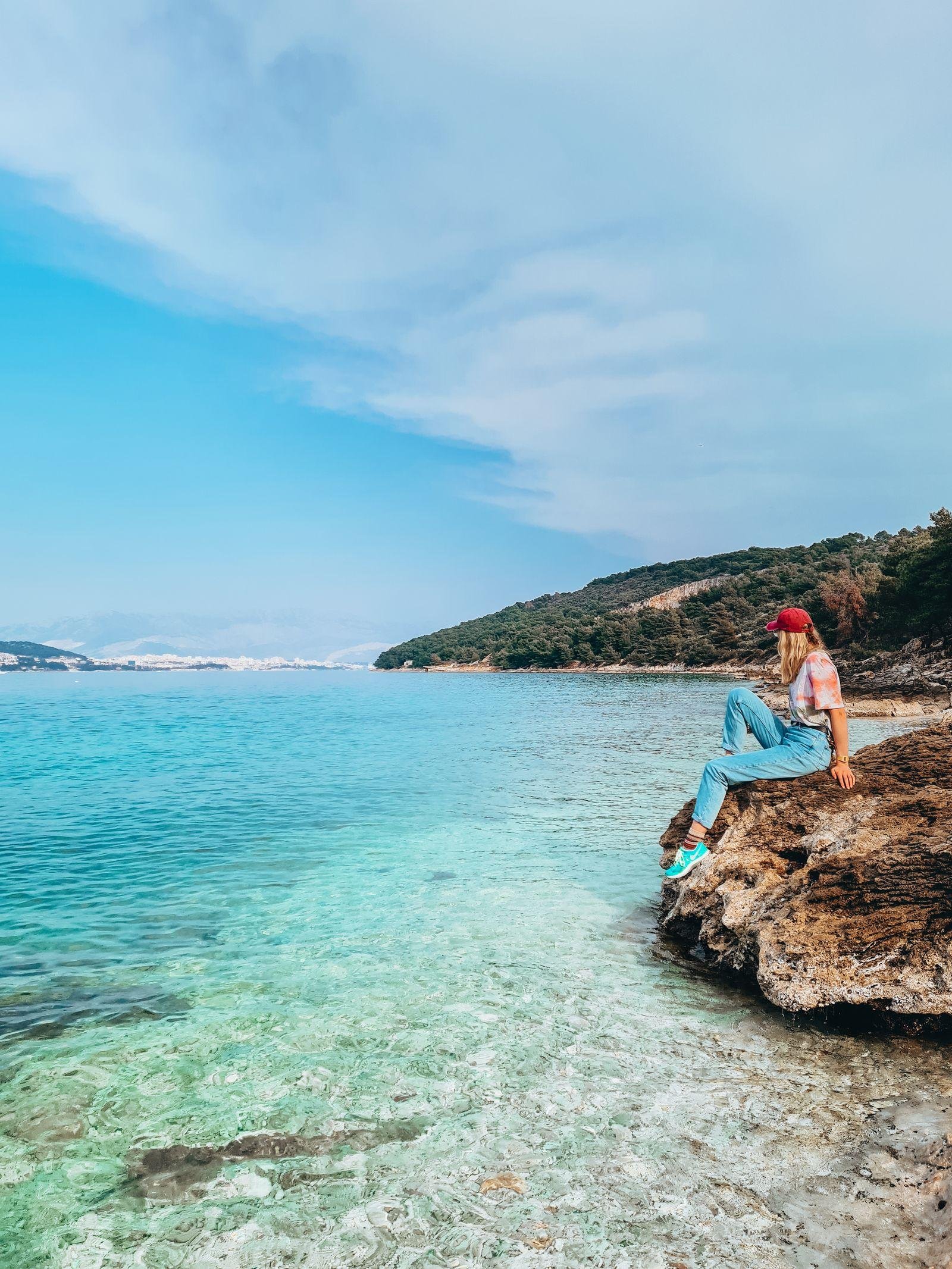 girl sitting on a rock beside clear turquoise water in a bay